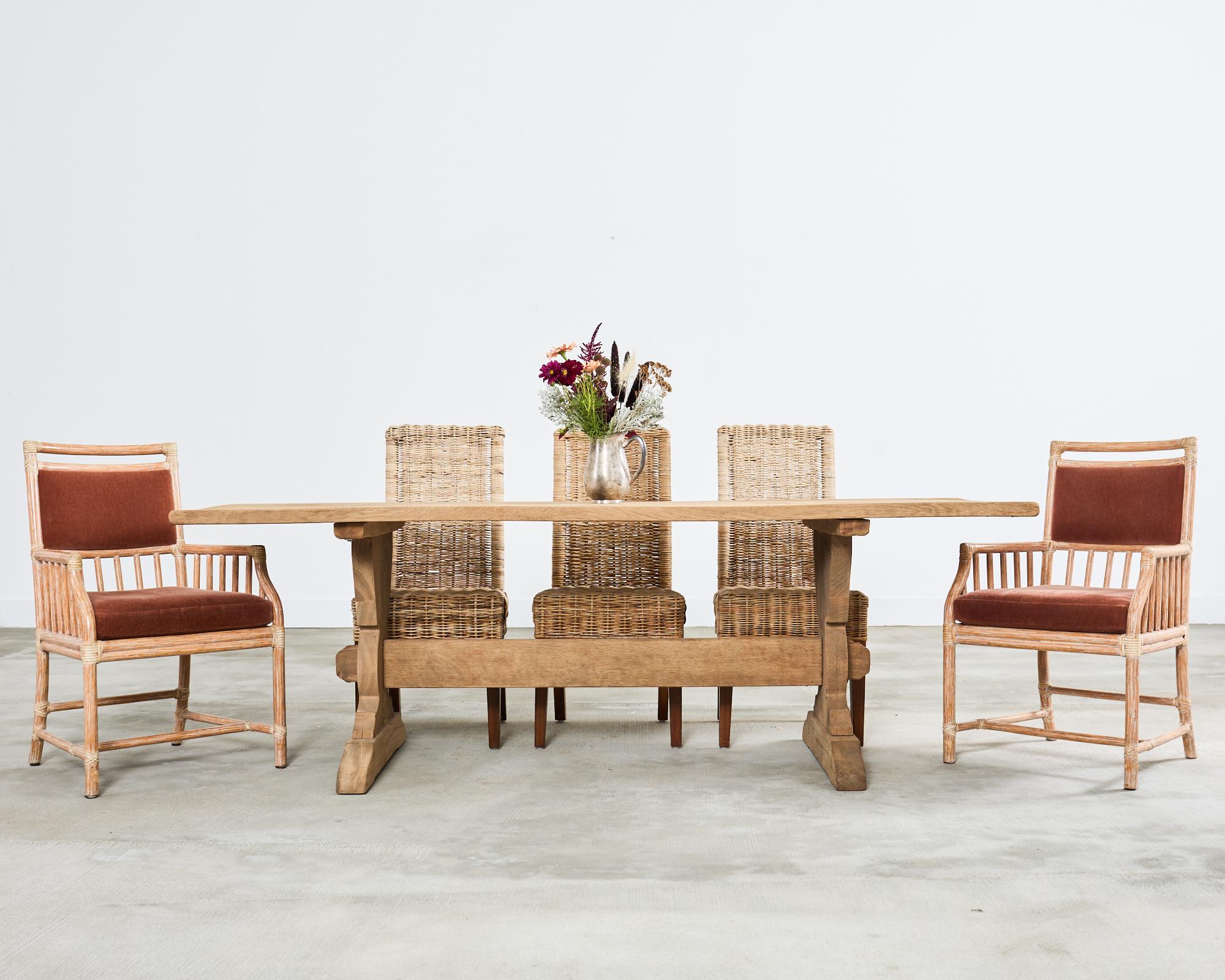 Rustic 20th century country French farmhouse trestle dining table featuring a bleached oak finish. The table has a thick rectangular plank top supported by a trestle style base. The shaped legs are conjoined by a long stretcher having mortise and