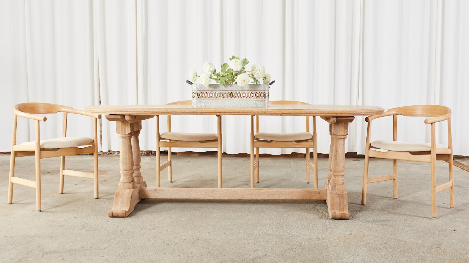 Substantial country French trestle dining table featuring a bleached oak finish. Heavy and solid crafted from solid oak with a nearly 2 inch thick plank top in an elongated oval form. Constructed with wood peg joinery the top is supported by double