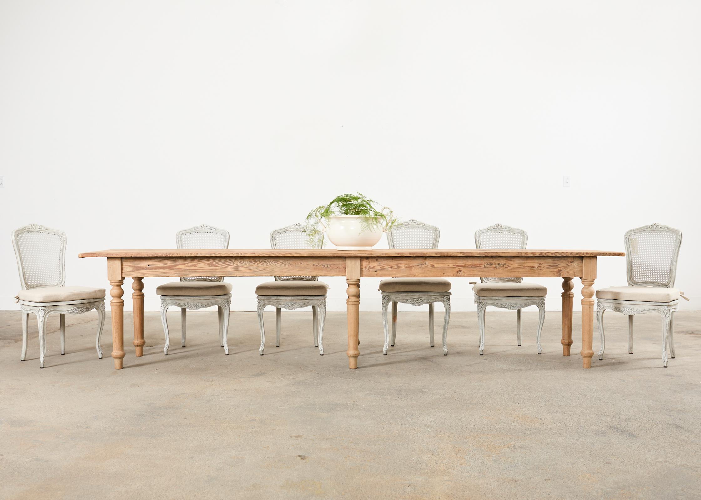 Monumental country French farmhouse harvest vineyard table, dining table, or console table measuring nearly 12 feet long. The table features a 1 inch thick scrubbed pine plank top with breadboard ends. The finish has been stripped on the pine and