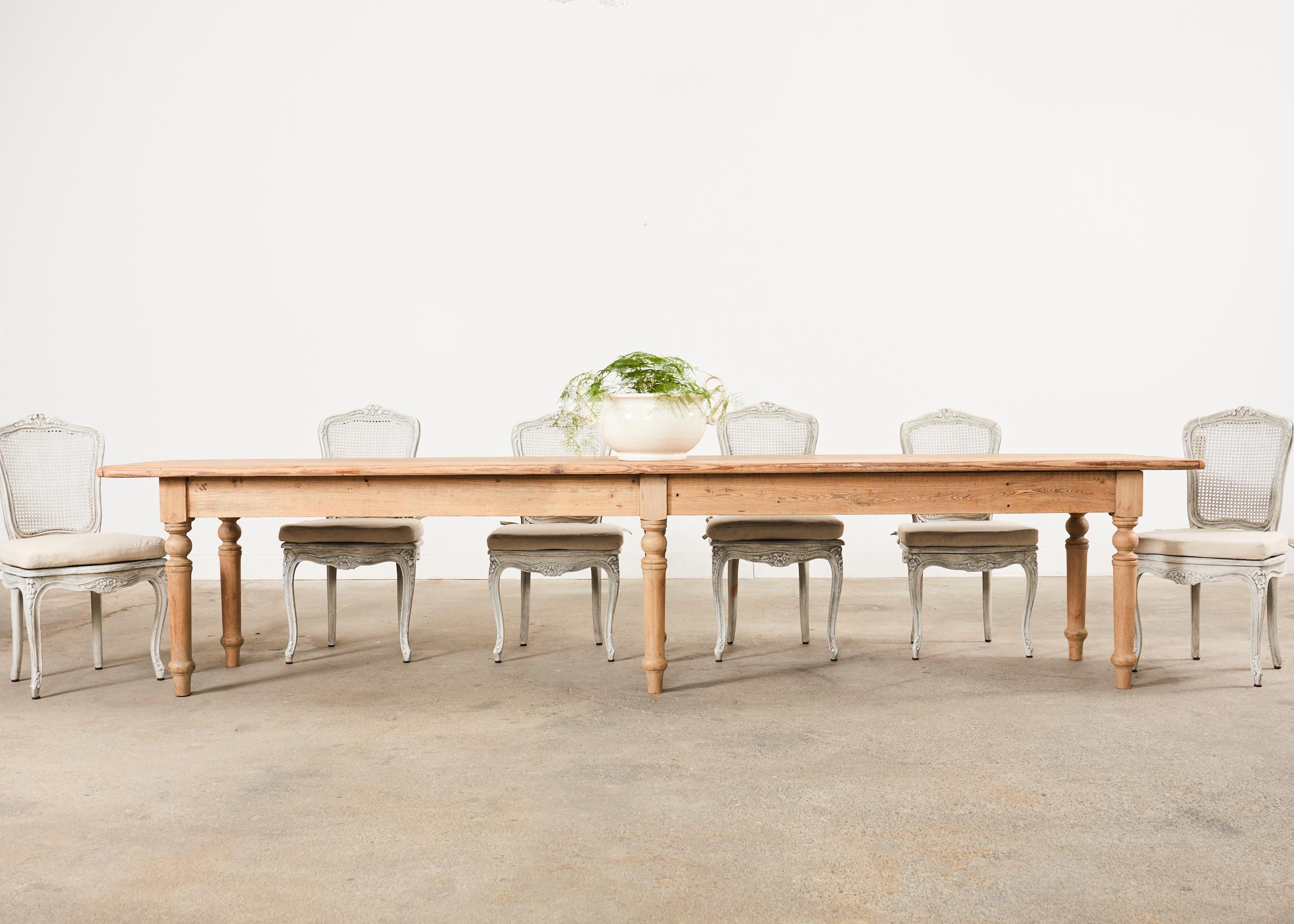 Monumental country French farmhouse harvest vineyard table, dining table, or console table measuring nearly 12 feet long. The table features a 1 inch thick scrubbed pine plank top with breadboard ends. The finish has been stripped on the pine and