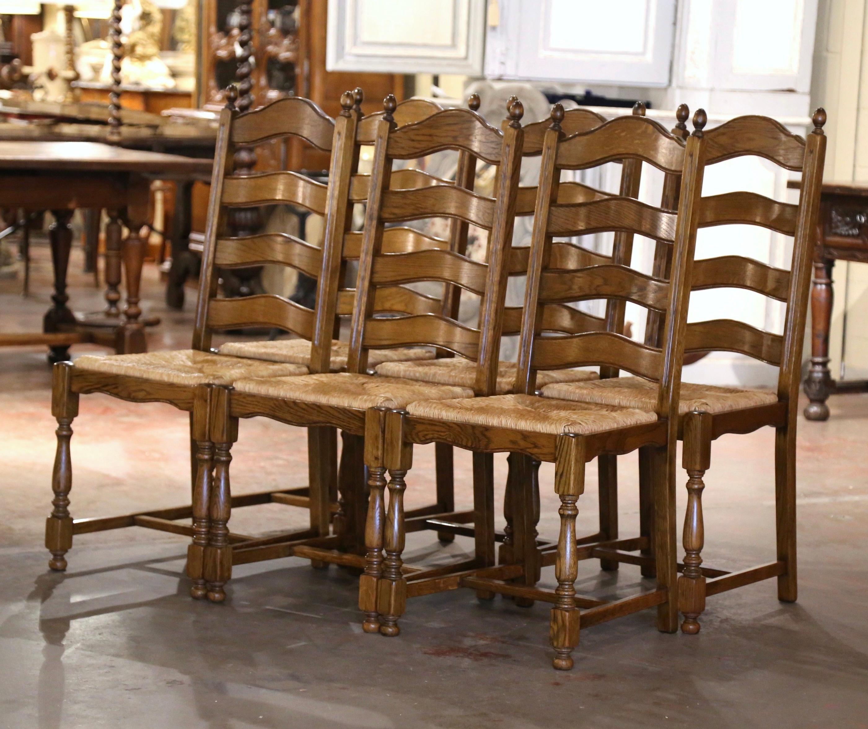 These six elegant country chairs were crafted in Normandy France, circa 2000. Carved from solid oak, each chair stands on turned front legs and back legs, all connected with a bottom stretcher. Each chair has a tall pitched back with four scalloped