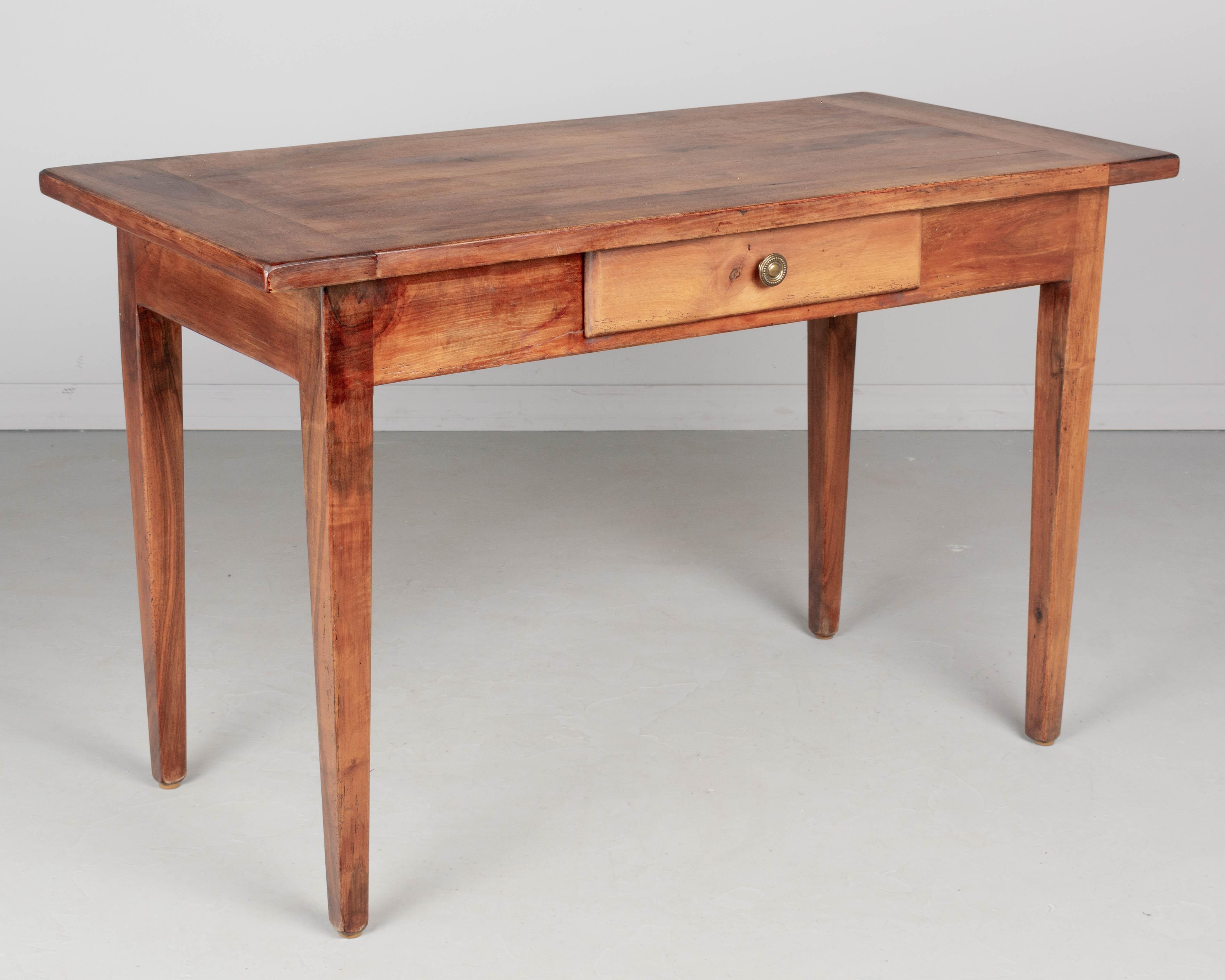 A small Country French farm table made of solid walnut with tapered legs and a dovetailed drawer with brass knob. Pegged construction. Waxed finish. A good sturdy table with normal wear for its age and use. Perfect for use as a desk. Circa