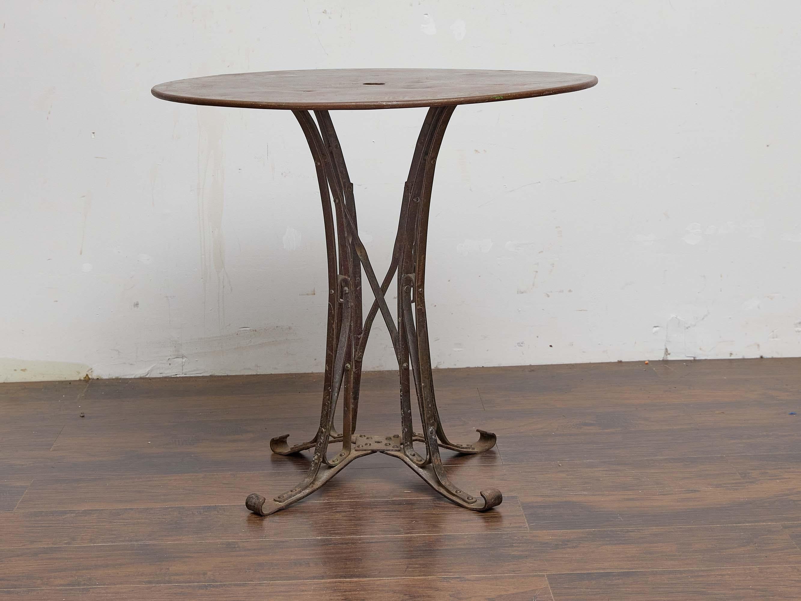 Esta mesa de jardín Country French de hierro, de principios del siglo XX, hacia 1920, capta el espíritu intemporal de la vida al aire libre en la Francia provinciana. Su parte superior circular, perforada en el centro para alojar una sombrilla,