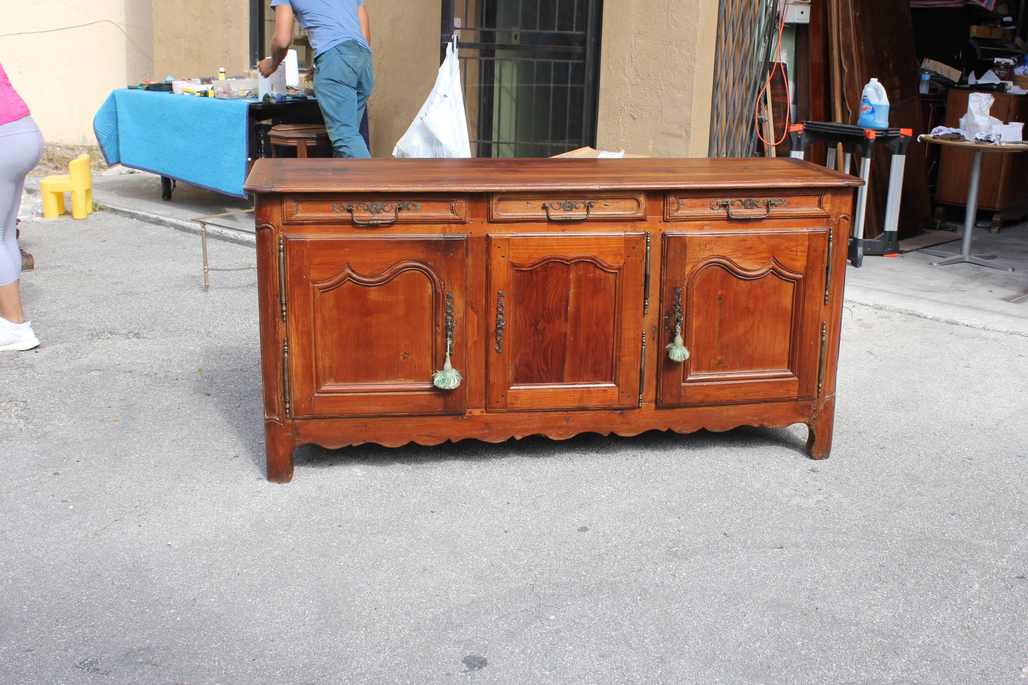 Charming, large country French Louis XV period chateau sideboard handcrafted of solid and beautifully patinated cherry by talented artisans from south France, consisting of a shaped top sitting upon an elegant facade boasting three drawers, each