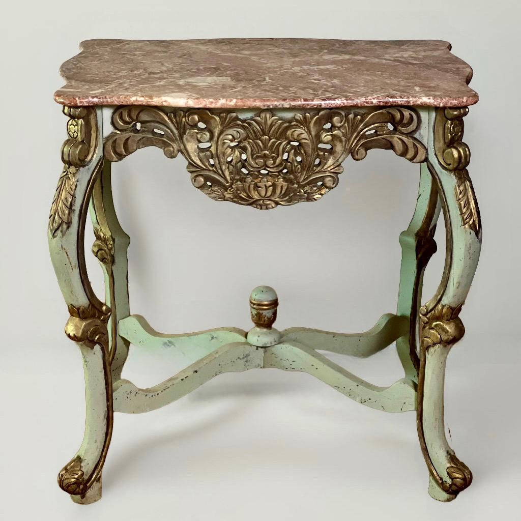 Country French center table or console carved and painted in pale sage green with a rouge marble top and gilt wood accents, c. 1940s.

A stunning table with a serpentine marble top having variations of green and white set upon a broad foliate