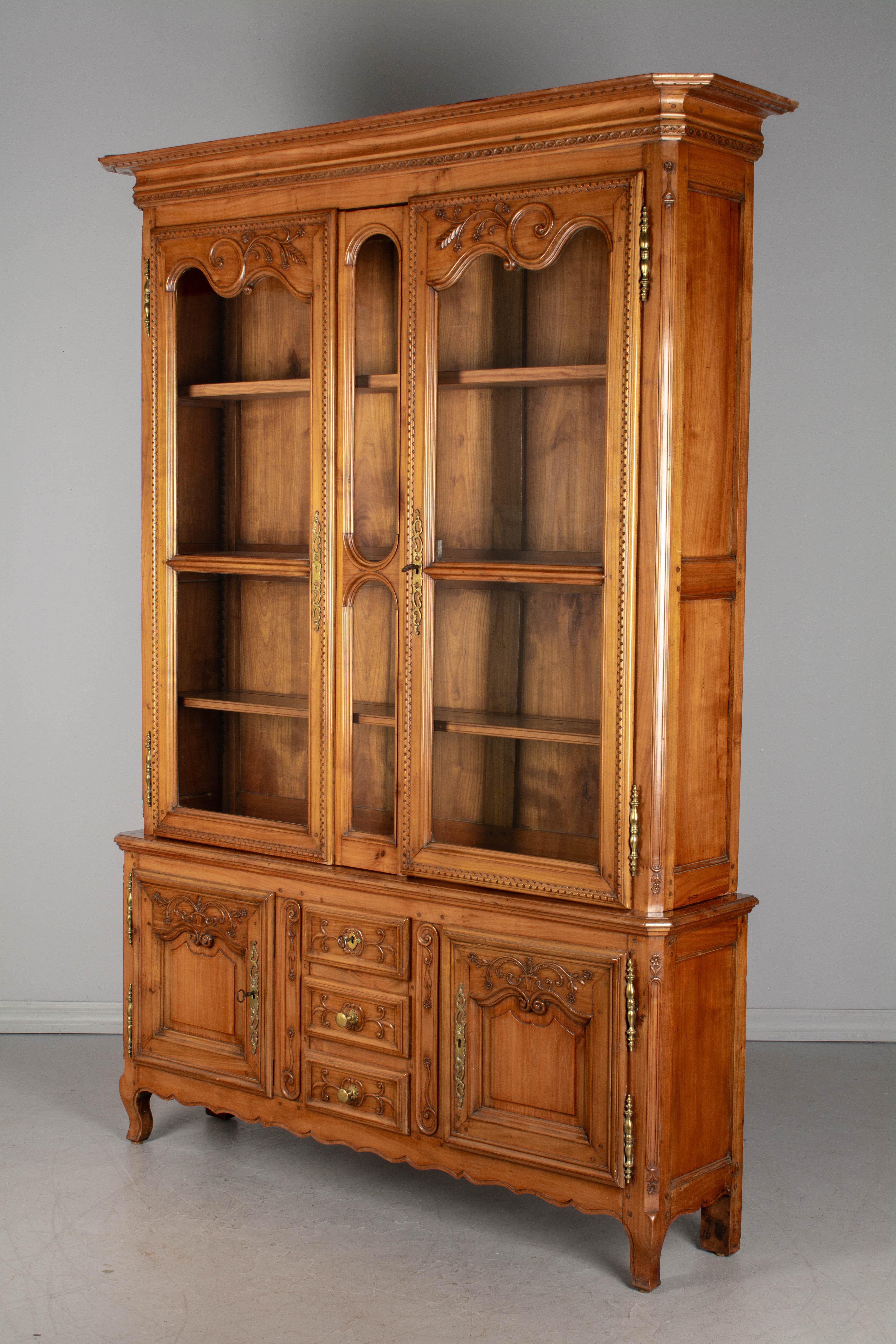 A Country French Louis XV style vitrine, or China cabinet from Northern France. Made of solid cherrywood with hand carved decoration. In two parts, the bottom has two doors with working locks & key and three dovetailed drawers. The glass paned