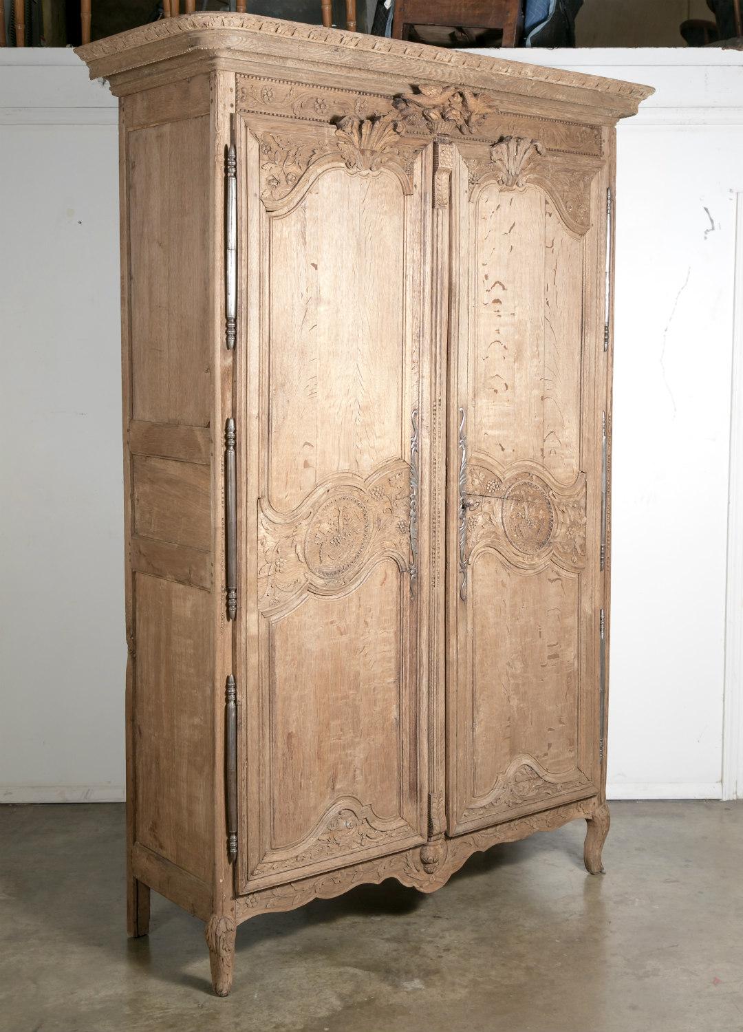 Antique country French Louis XV style washed oak Normandy marriage armoire having a large flat, molded cornice that sits upon a carved frieze featuring a pair of love birds and a basket of flowers. The paneled doors highlighted with floral and