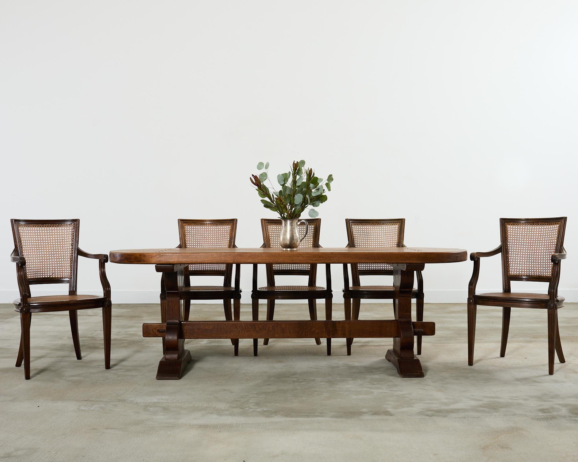 Substantial country French farmhouse dining table featuring round demi-lune ends. The table features a 2.5 inch thick top crafted from large oak timbers. The top is supported by a trestle base having hourglass form legs ending with 5.5 inch thick