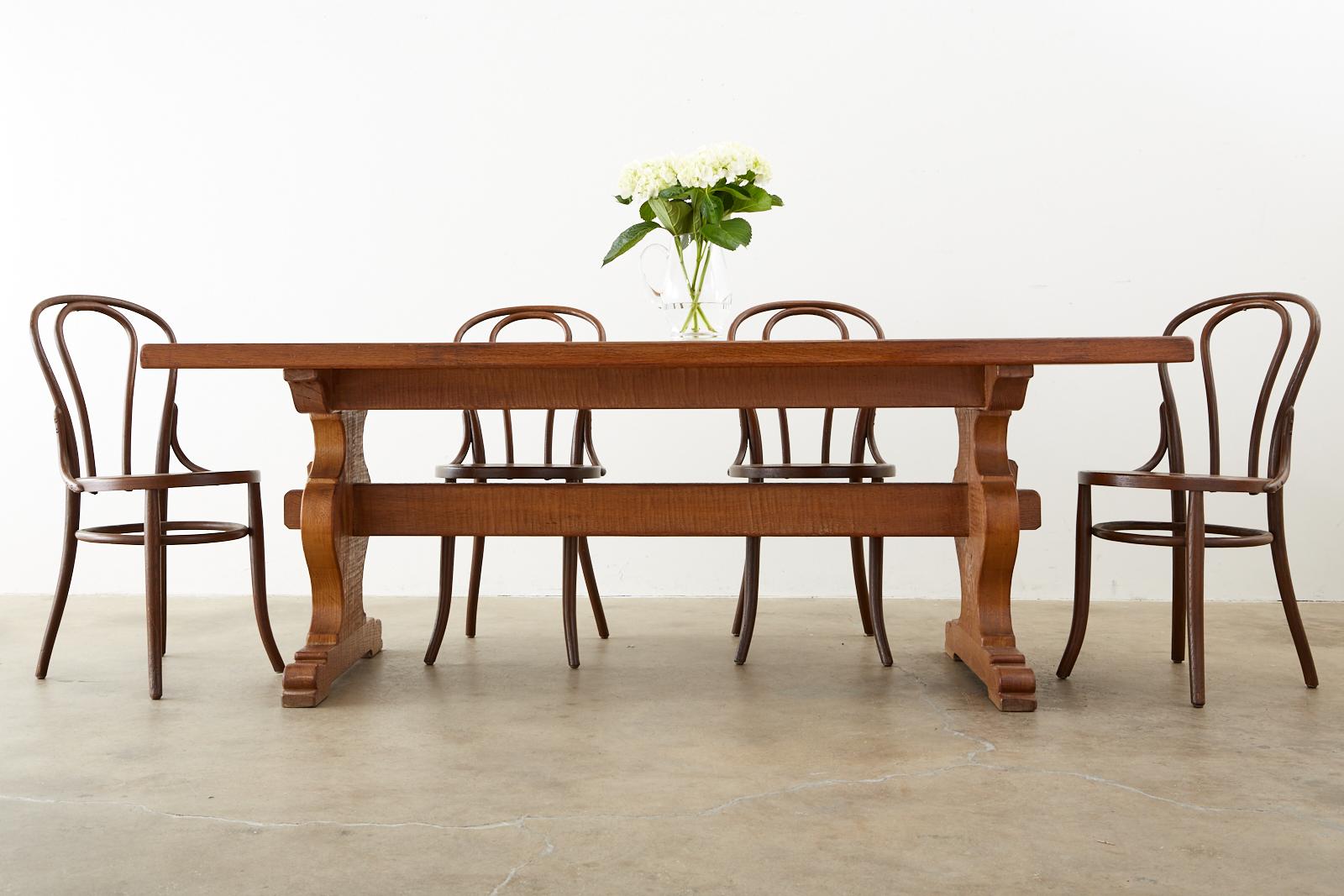 Rustic country French farmhouse trestle dining table constructed from oak. The table features a 2 inch thick solid oak top supported by beautifully shaped trestle legs ending with shoe feet. The legs are conjoined by a stretcher having an exposed