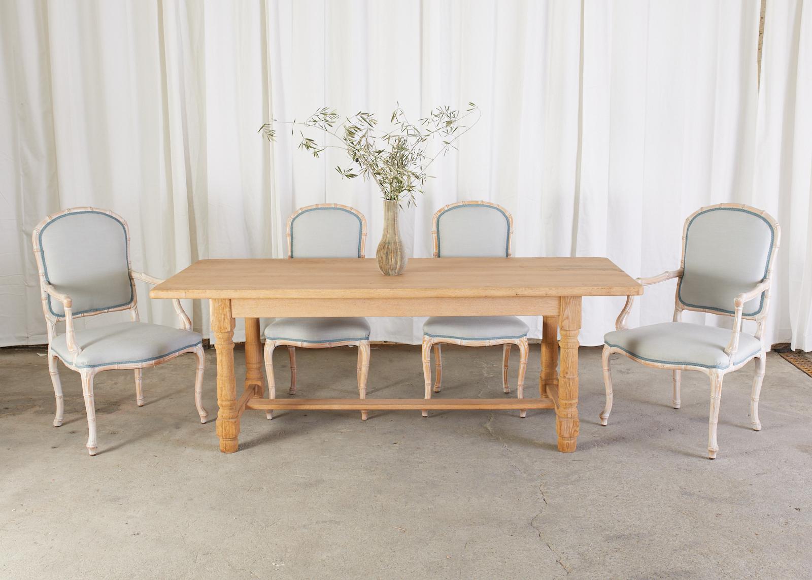 Rustic Country French farmhouse dining table or harvest table featuring a bleached oak distressed finish with an aged patina. Constructed with a 1.5 inch thick plank top of solid oak. Ample legroom measuring 24.5 inches from the floor to the apron.