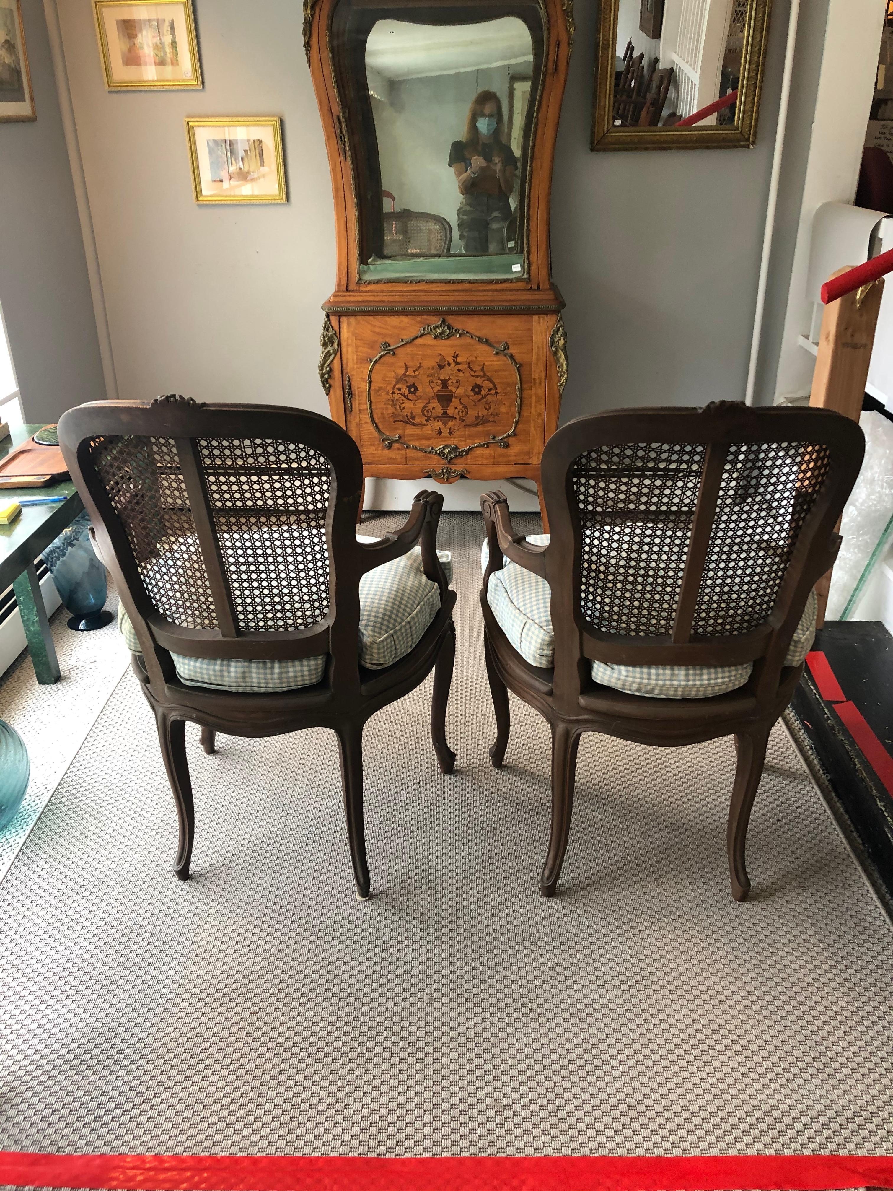 Elegant yet casual pair of comfy French carved walnut armchairs having caned seats and backs, window pane back, and custom light blue and white checked down filled seat cushions. Would work well at each end of a dining table.
Measures: Arm height