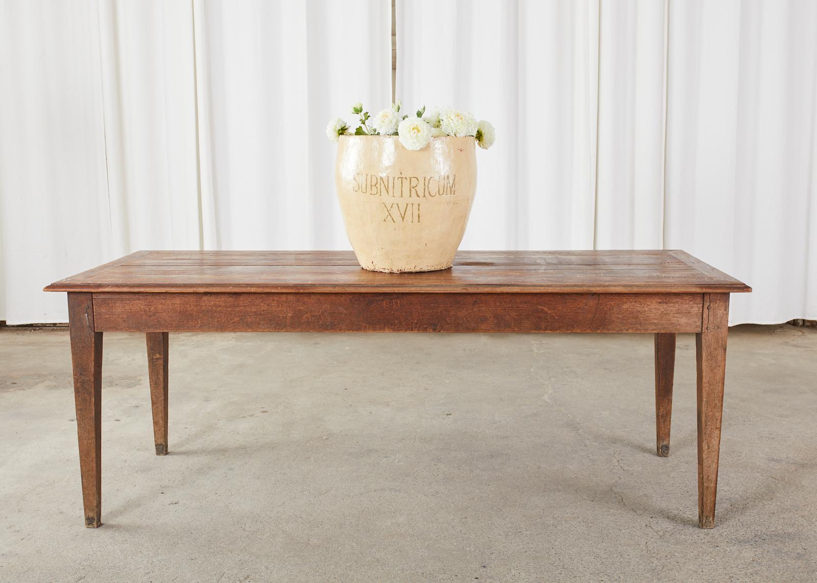 Rustic country French farmhouse harvest table or dining table crafted from pine and oak. The table features a framed plank top made of pine with an ogee edge. The base appears to be crafted from oak with wood peg joinery. Ample leg room measuring