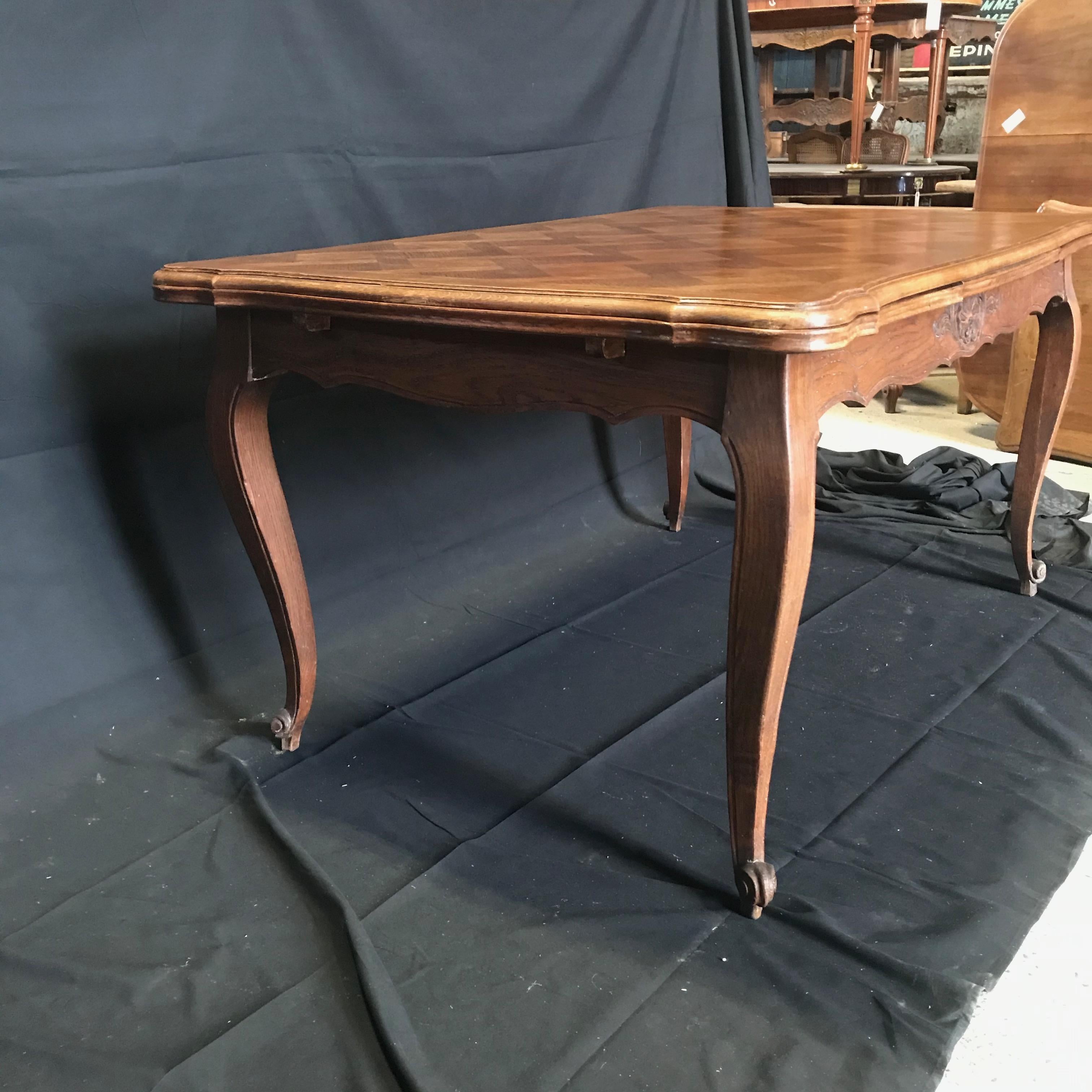 Beautifully carved French country farmhouse extension table featuring a parquetry inlay top and two inset leaves. This versatile table has carved cabriolet legs terminating in snail's head feet, with scroll and shell carvings on the apron. With