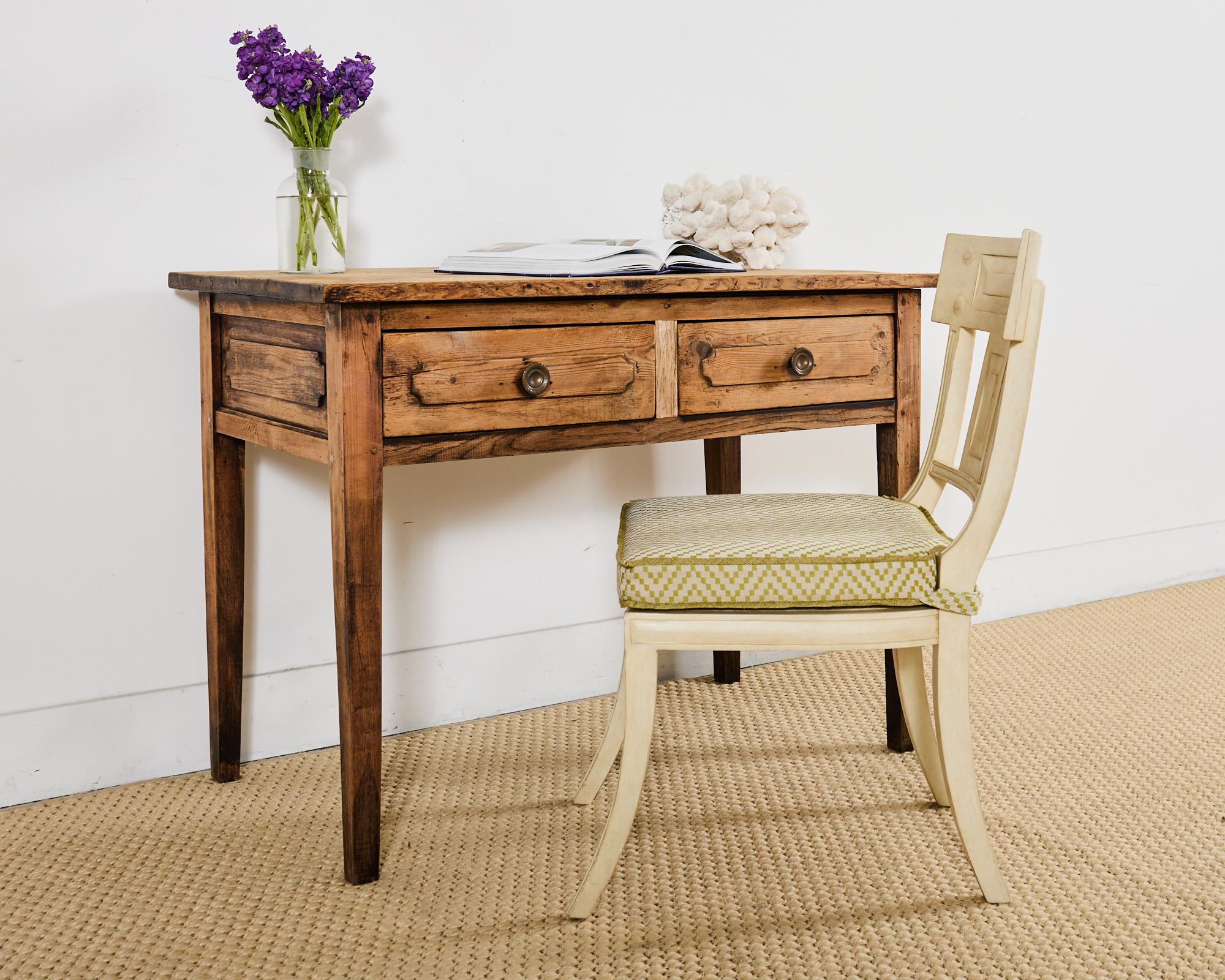 Weathered country French provincial writing table, desk, or console featuring a stripped, bleached finish. The table has a one inch thick rectangular plank top and is fronted by two large storage drawers. The drawers have patinated brass pulls and