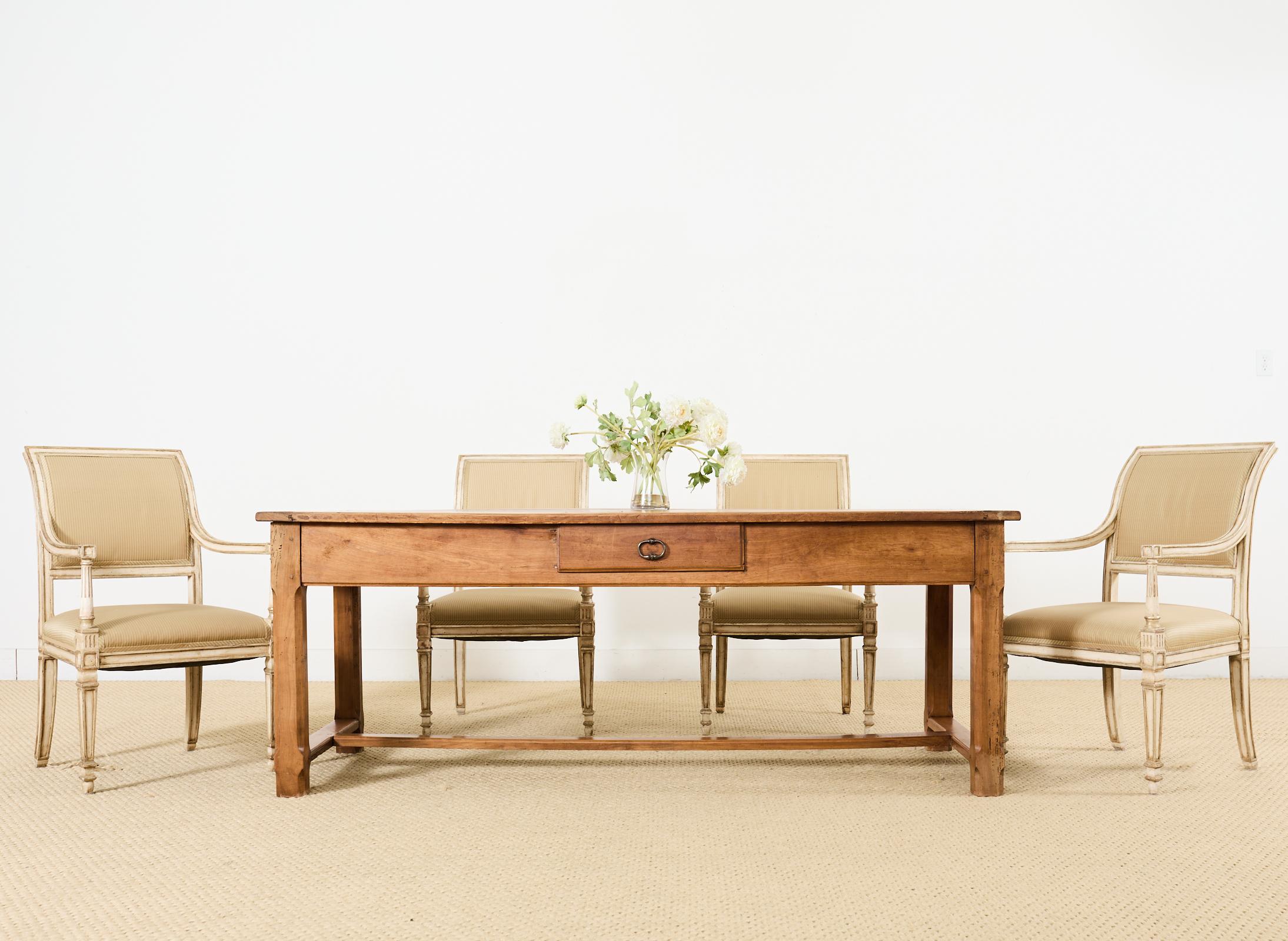 Quintessential country French provincial farmhouse trestle dining table hand-crafted from warm radiant fruitwood. The table features a thick plank top with breadboard ends. Constructed with wood peg joinery the trestle base has 2 storage drawers in