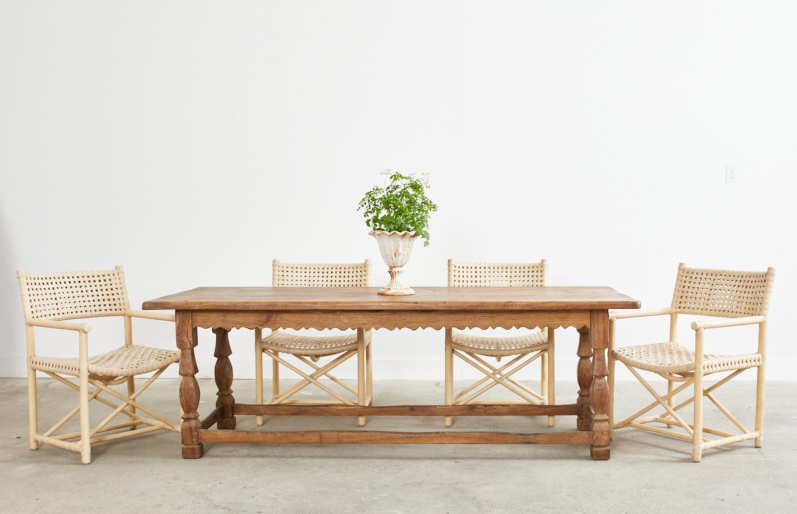 Rustic 19th century country French provincial farmhouse harvest or dining table hand-crafted from oak. The table features a trestle style base with a whimsical scalloped apron on all sides. The table is supported by shaped square legs conjoined by