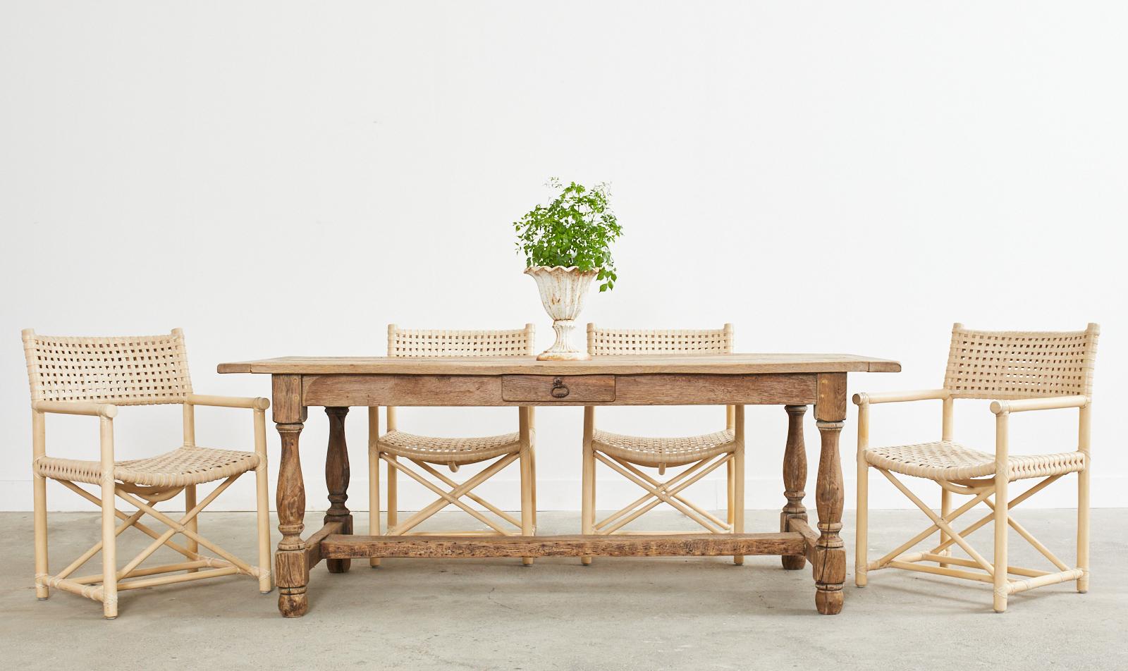 Rustic and elegant country French provincial farmhouse trestle dining table featuring an older bleached oak finish. Amazing patina with a desirable weathered, and distressed finish. Solid and strong thick plank top with breadboard ends supported by