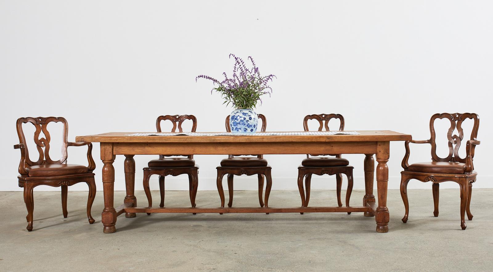 Handsome country French provincial farmhouse dining table or harvest table featuring a 2 inch thick oak plank top with peg joinery. The top is supported by a trestle style base with thick turned legs. The legs are conjoined by long stretchers. Very