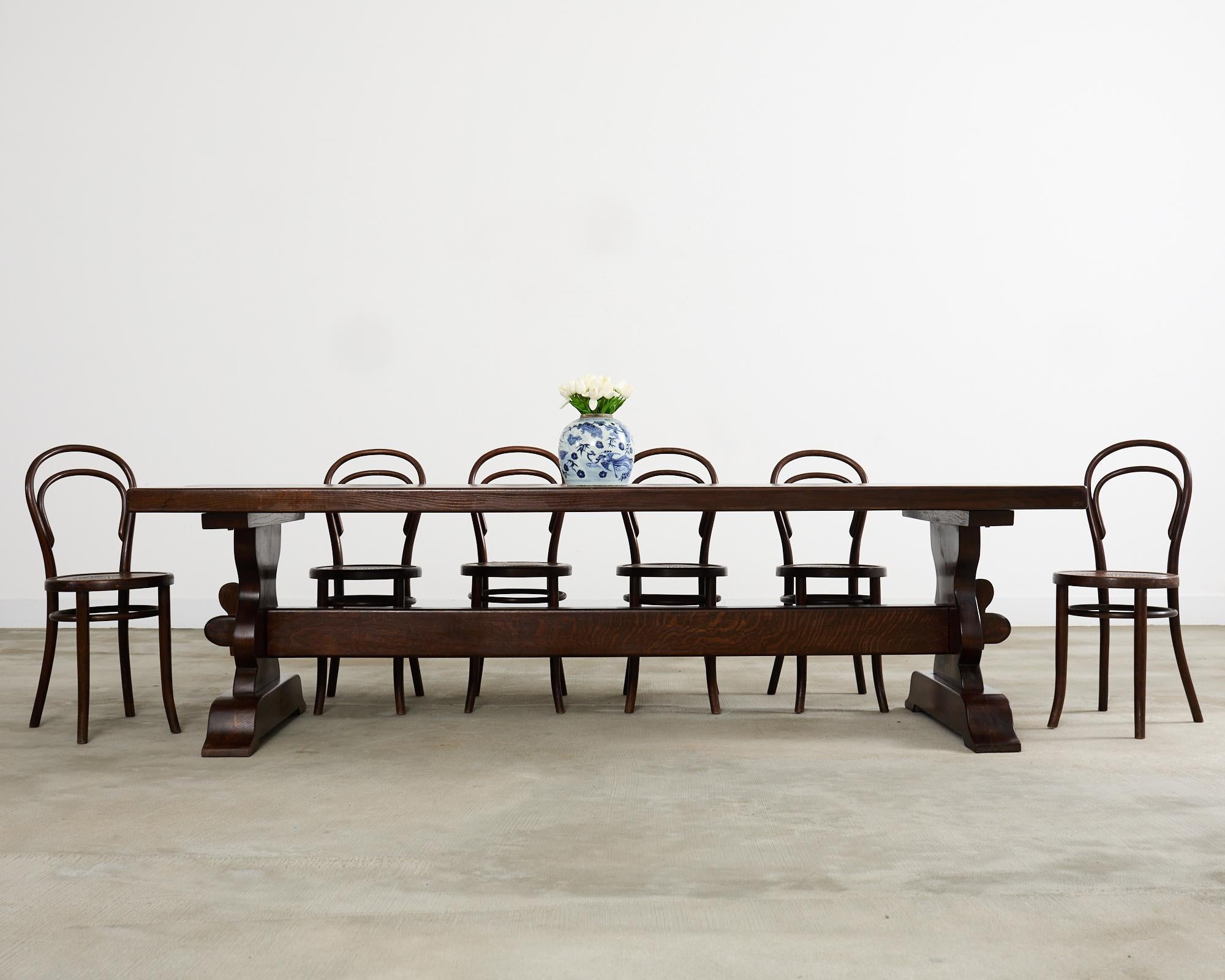 Grand country French provincial farmhouse dining table crafted from solid oak timbers. The massive table is made in a monastery style and features a 104 inch long rectangular top that measures nearly 3 inches thick. The top is supported by a trestle