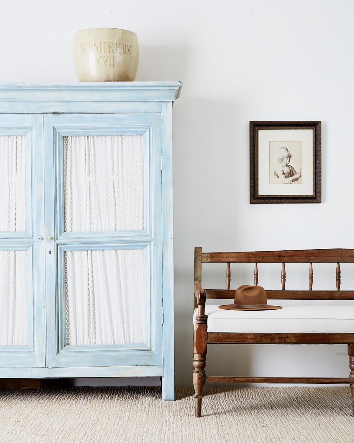 Rustic country French armoire cabinet made in the Provincial style. Features a beautiful French blue painted finish with a distressed and faded patina. The two large doors have a farmhouse style chicken wire in the windows and are fitted with