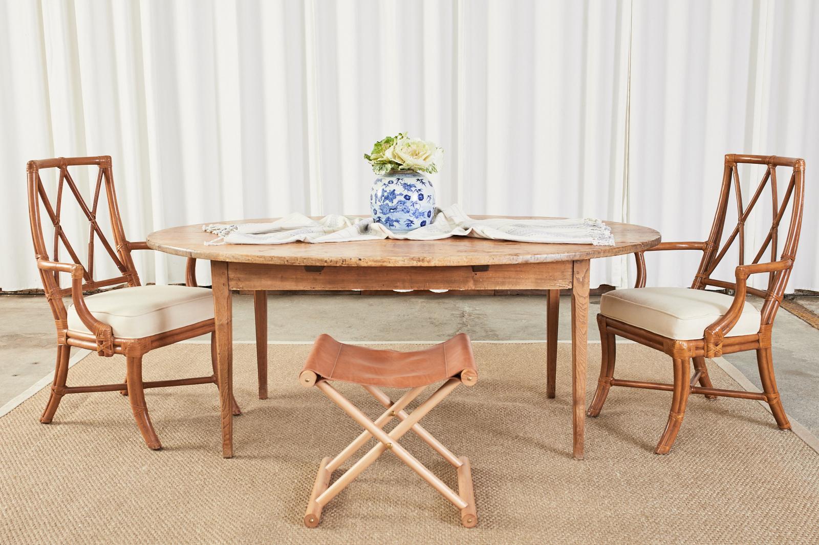 Early 19th century country French provincial farmhouse dining table featuring a patinated oval plank top. The top is crafted from 1 inch thick boards having tongue and groove joinery. The top is supported by a fruitwood base and later added oak legs