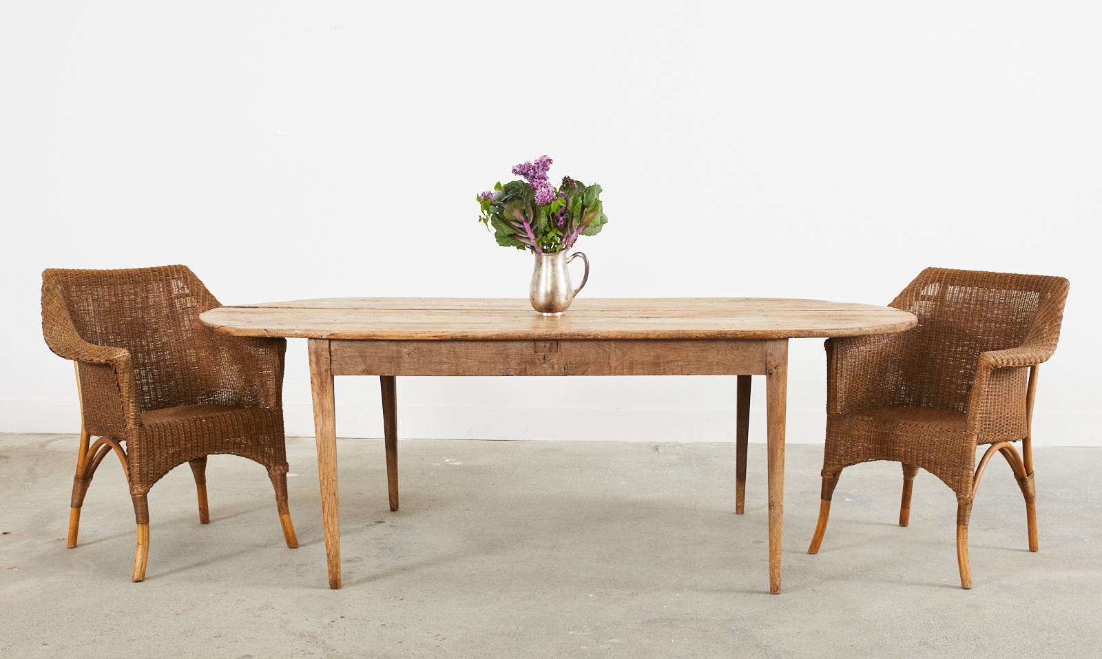 Rustic early 19th century country French provincial farmhouse dining table featuring a patinated oval plank top. The top is crafted from 1 inch thick soft pine boards with tongue and groove joinery. The top is supported by a fruitwood base and later