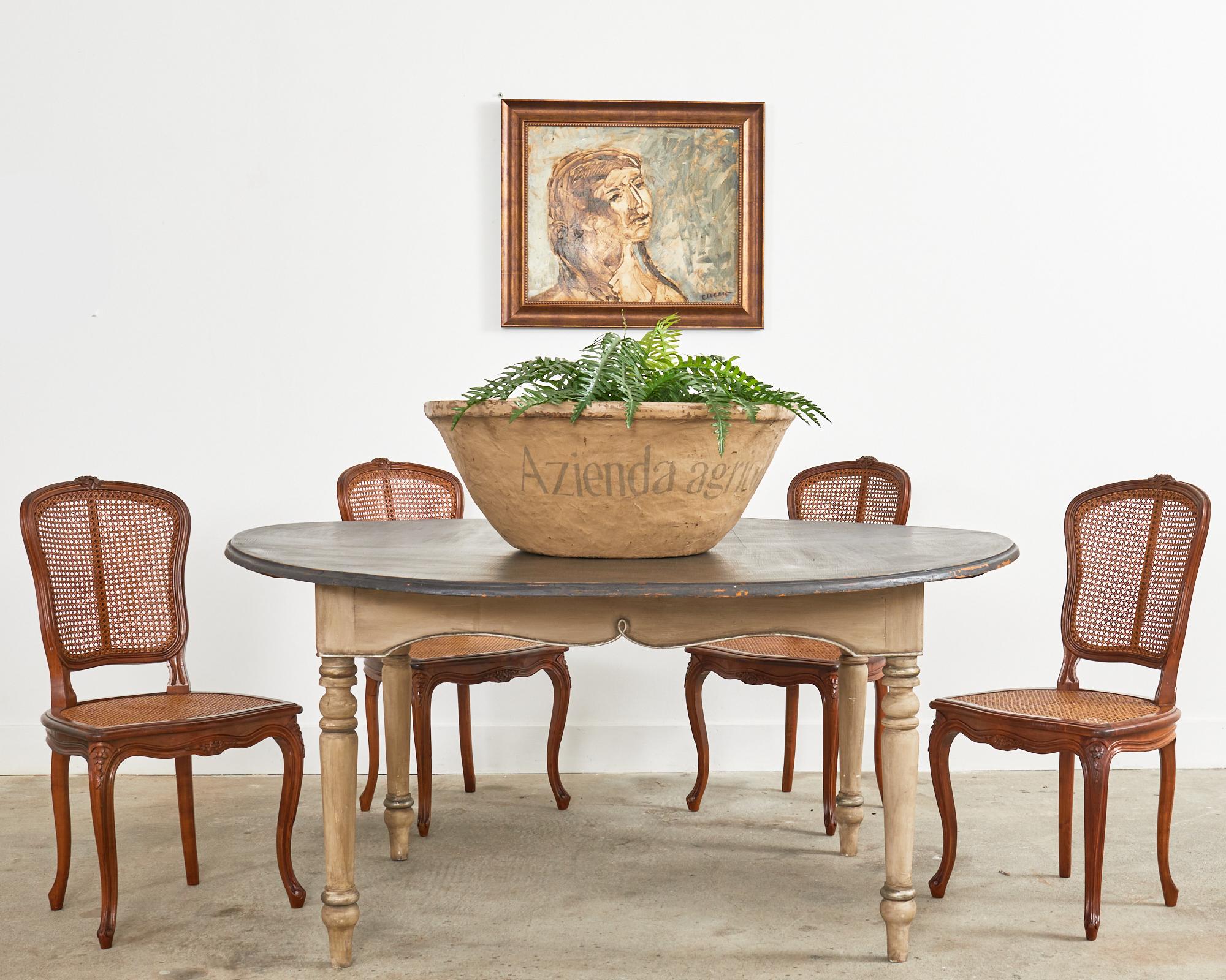 Rustic country french provincial round dining table painted by renowned Napa artist Ira Yeager (American 1938-2022) crafted from fruitwood. The table features an intentionally aged patina on the painted finish in a Swedish style with a grey base and