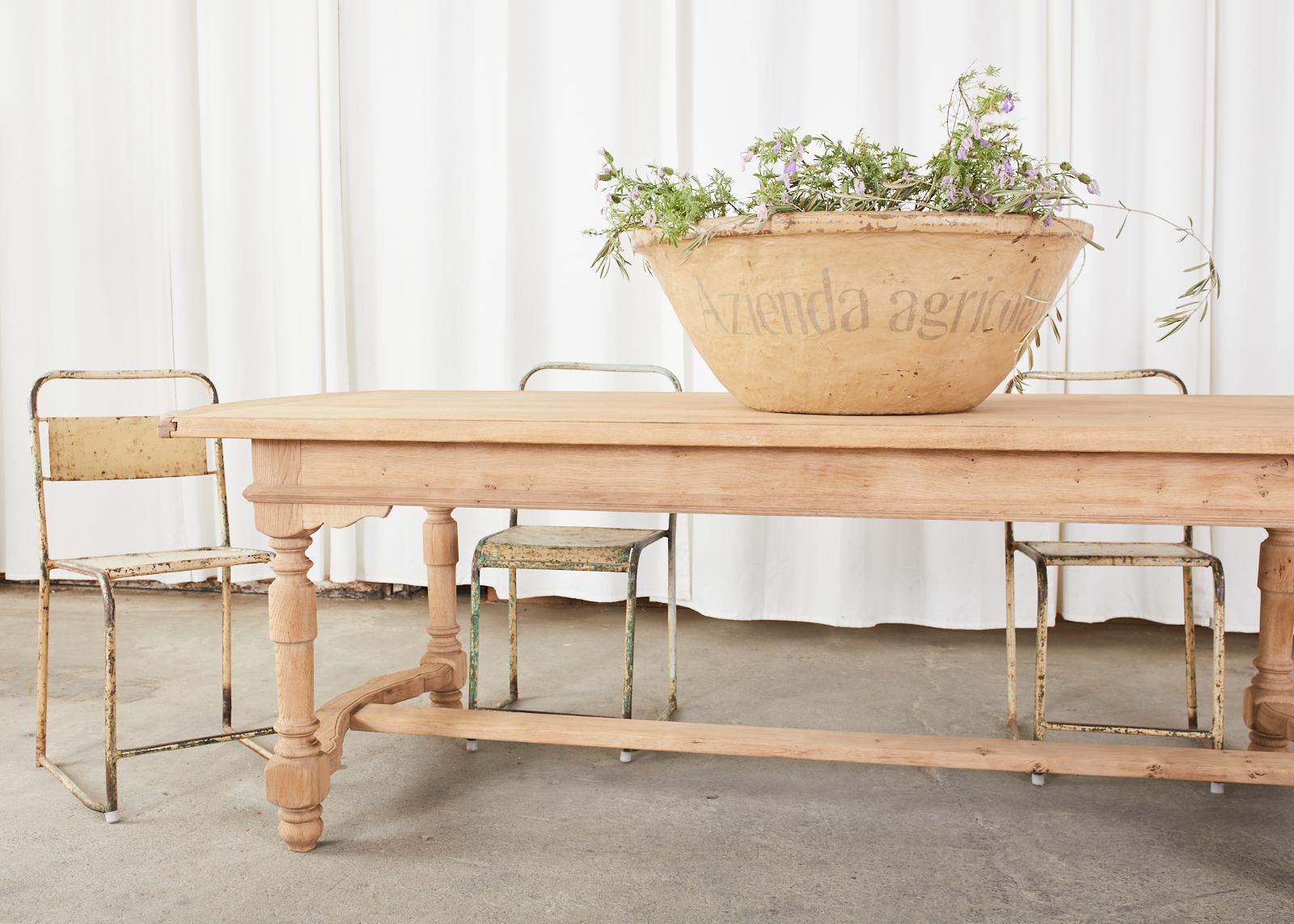 Rustic bleached oak farmhouse trestle dining table or harvest table made in the country French provincial style. The table features an intentionally stripped, bleached oak finish that gives the table character and charm. The top is crafted from 1.5