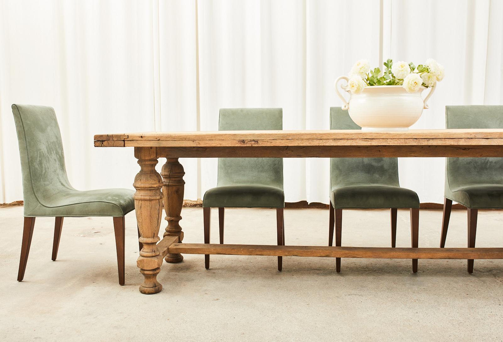 Magnificent country French provincial aged farmhouse style trestle dining table crafted from aged bleached oak. The massive table has a 2.5 inch thick plank top with tongue in groove breadboard ends. The top is supported by a substantial trestle