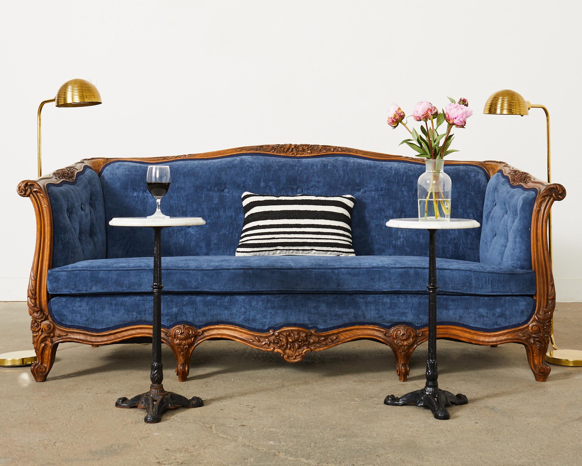 Opulent walnut canapé or sofa made in the country French provincial or Louis XV taste. The sofa features an elaborately carved case with scrolling acanthus and floral sprays. The frame is upholstered with a stunning French blue velvet giving the