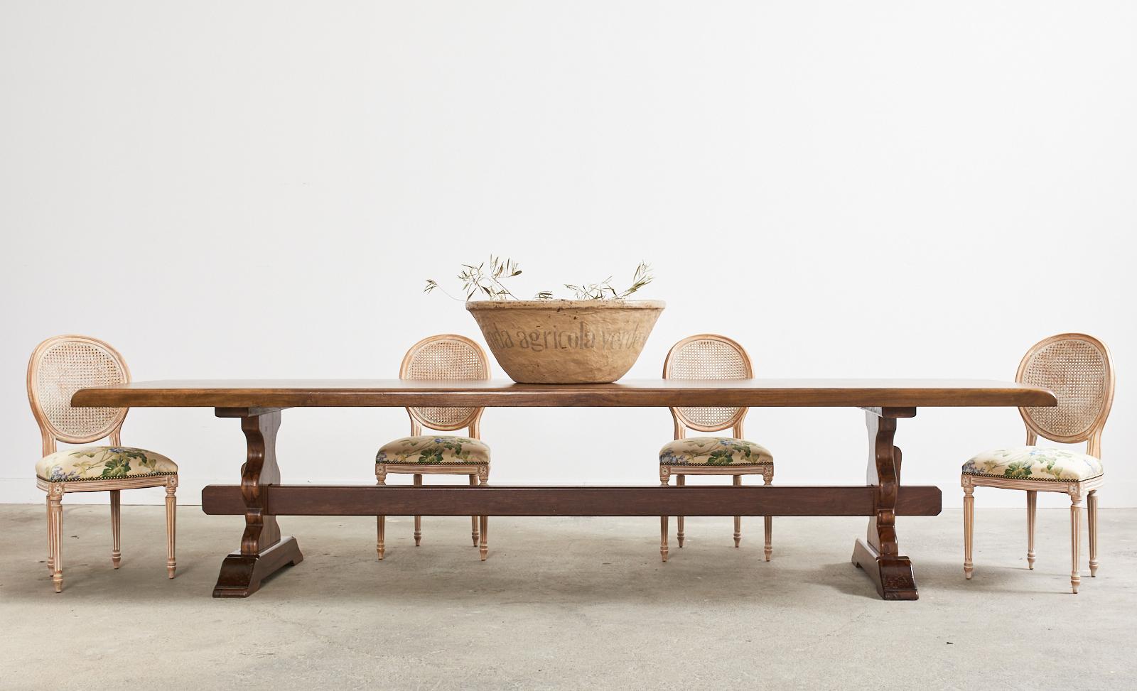 Monumental country French provincial style farmhouse dining table measuring 11.5 feet long. Beautifully crafted from rich walnut featuring a nearly 3 inch thick top. The large table is supported by a long trestle style base with hourglass shaped