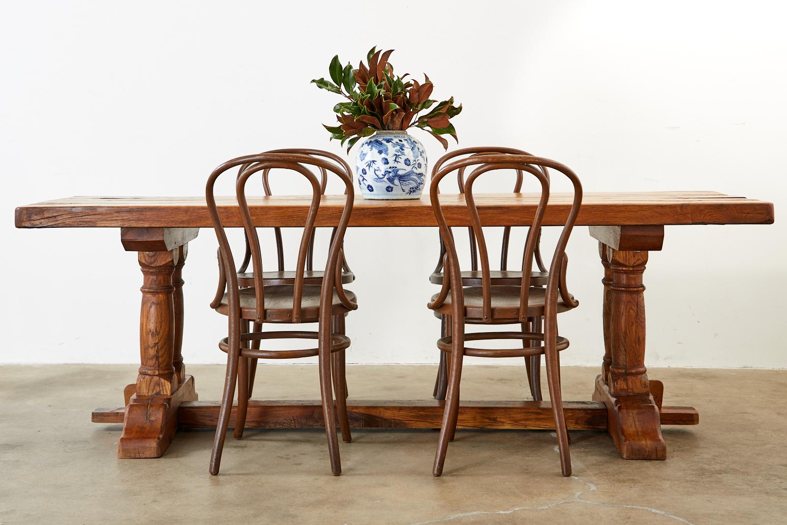 Rustic Country French farmhouse dining table featuring massive planks or reclaimed oak. The top measures 2.5 inches thick showcasing the antique wood grains and age. Supported by a massive trestle style base featuring thick column turned legs ending