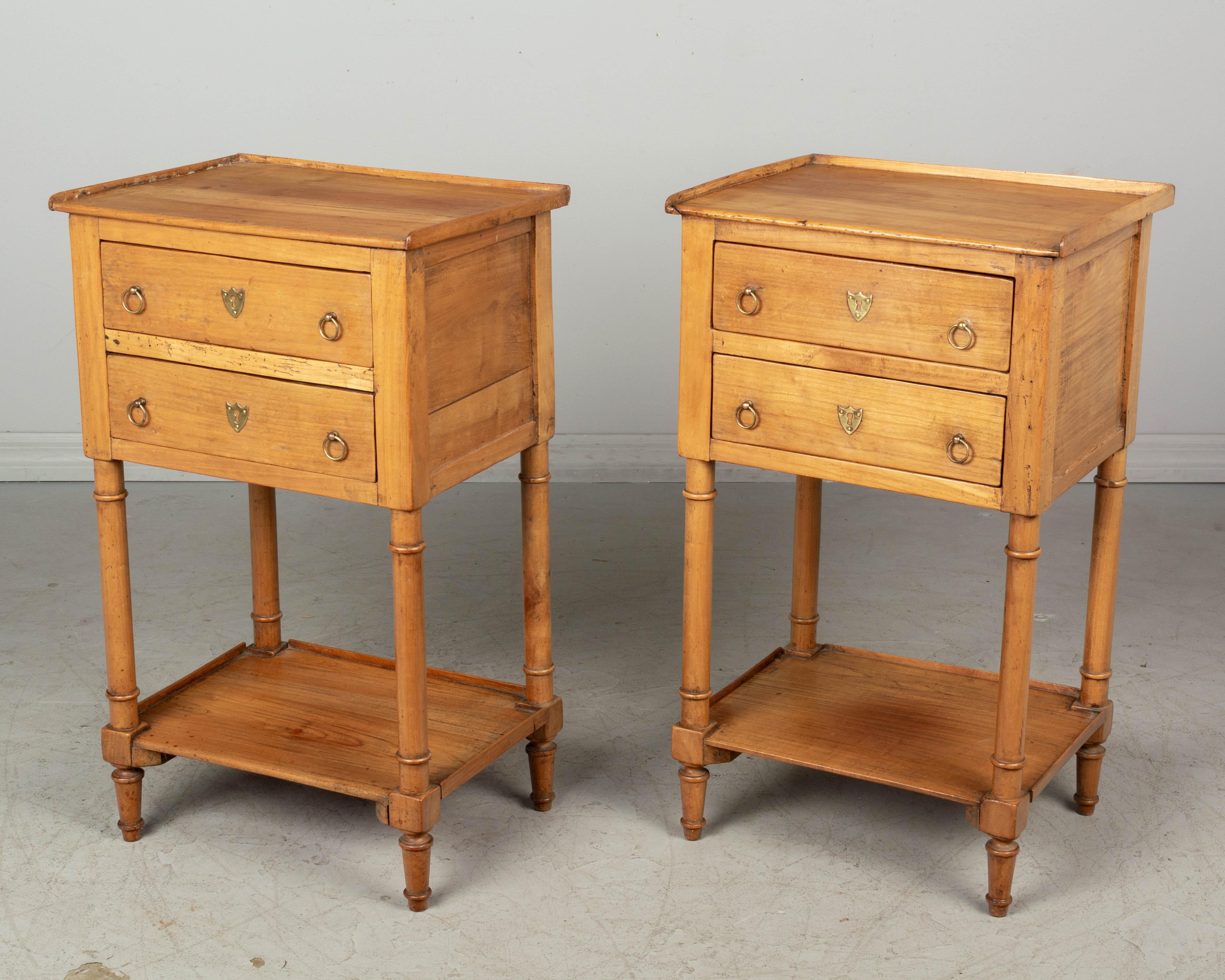 A pair of Country French Louis Philippe style side tables or nightstands made of cherrywood with turned legs and lower shelf. Two dovetailed drawers with brass ring pulls.