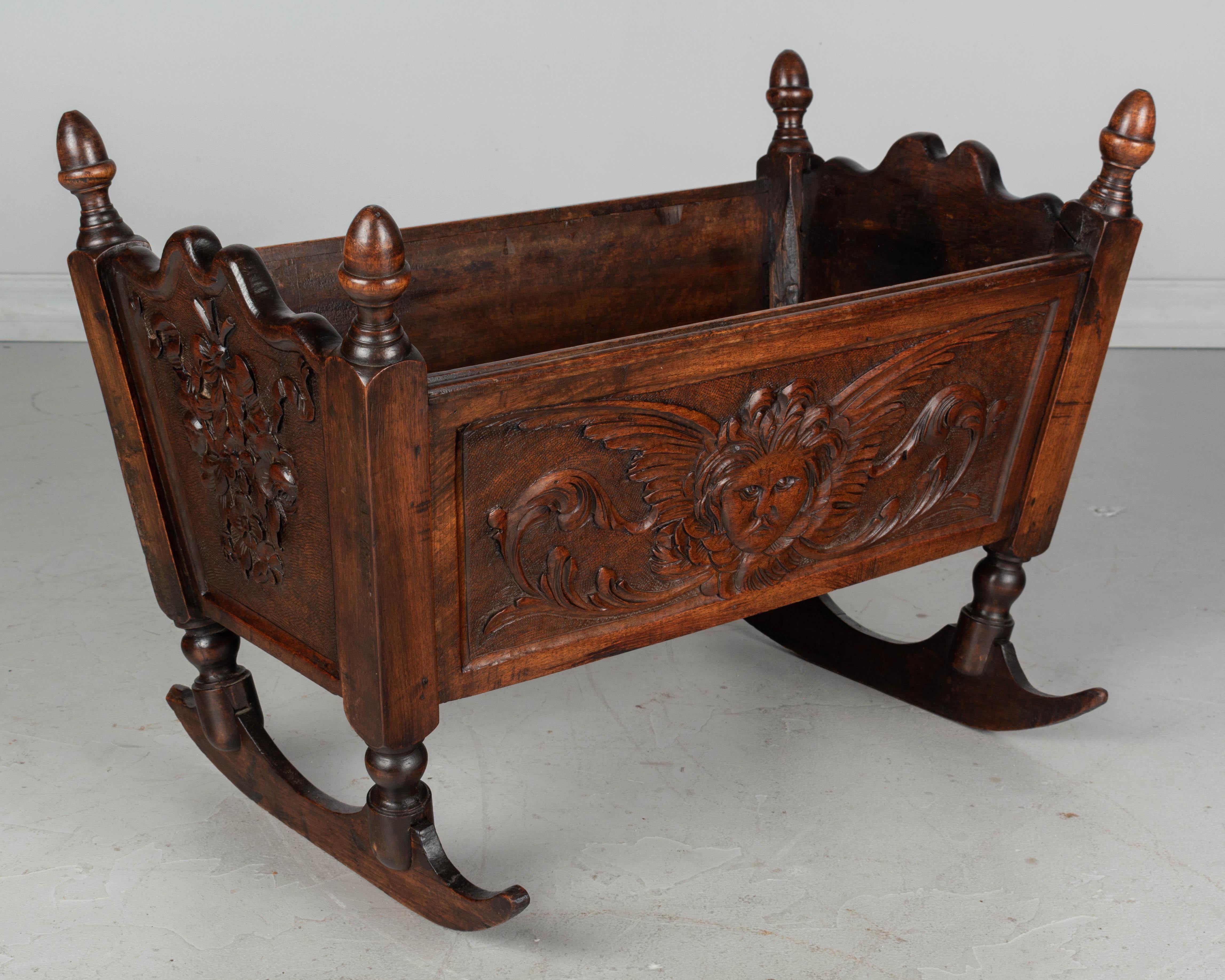 A 19th century country French baby cradle made of solid walnut with hand carved putti on both side panels and charming flower bouquets with ribbons carved on the ends. Accented with turned finials. May be used for dolls or converted into a planter