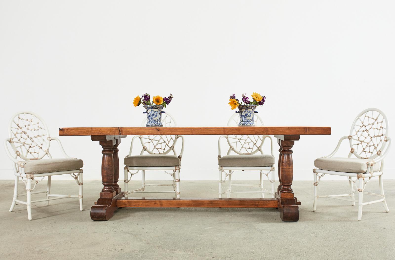 Imposing country French provincial farmhouse trestle dining table crafted from walnut. The table features a 2.5 inch thick walnut plank top with a warm honey toned finish. The large top is supported by a trestle base with double baluster form legs