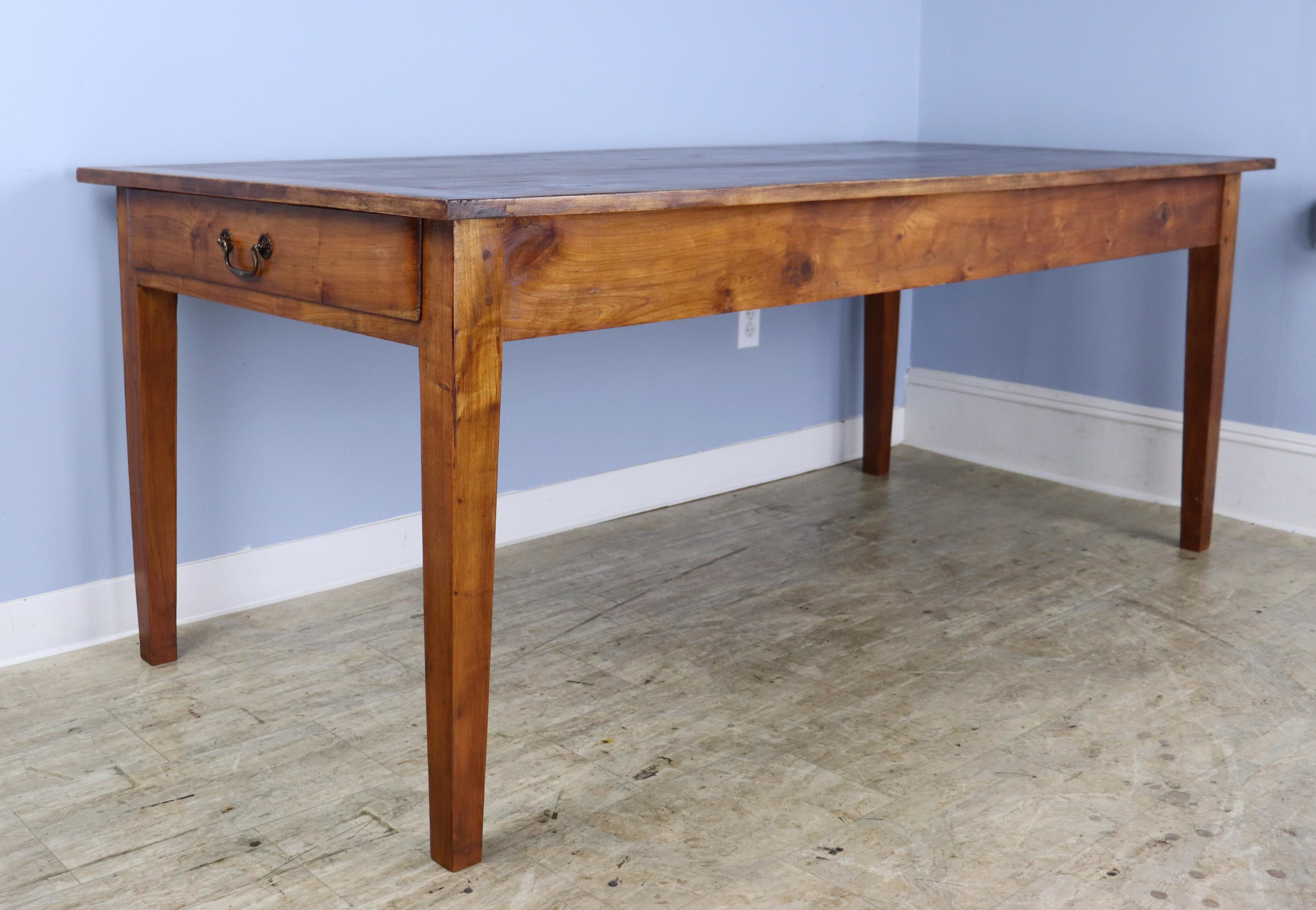 A simple and elegant fruitwood farm table with 72 inches between the legs on the long side. One drawer at one end and breadboard ends. Tapered legs, nicely pegged at the apron, which is 24.5 inches high. The table top has lots of good grain, with
