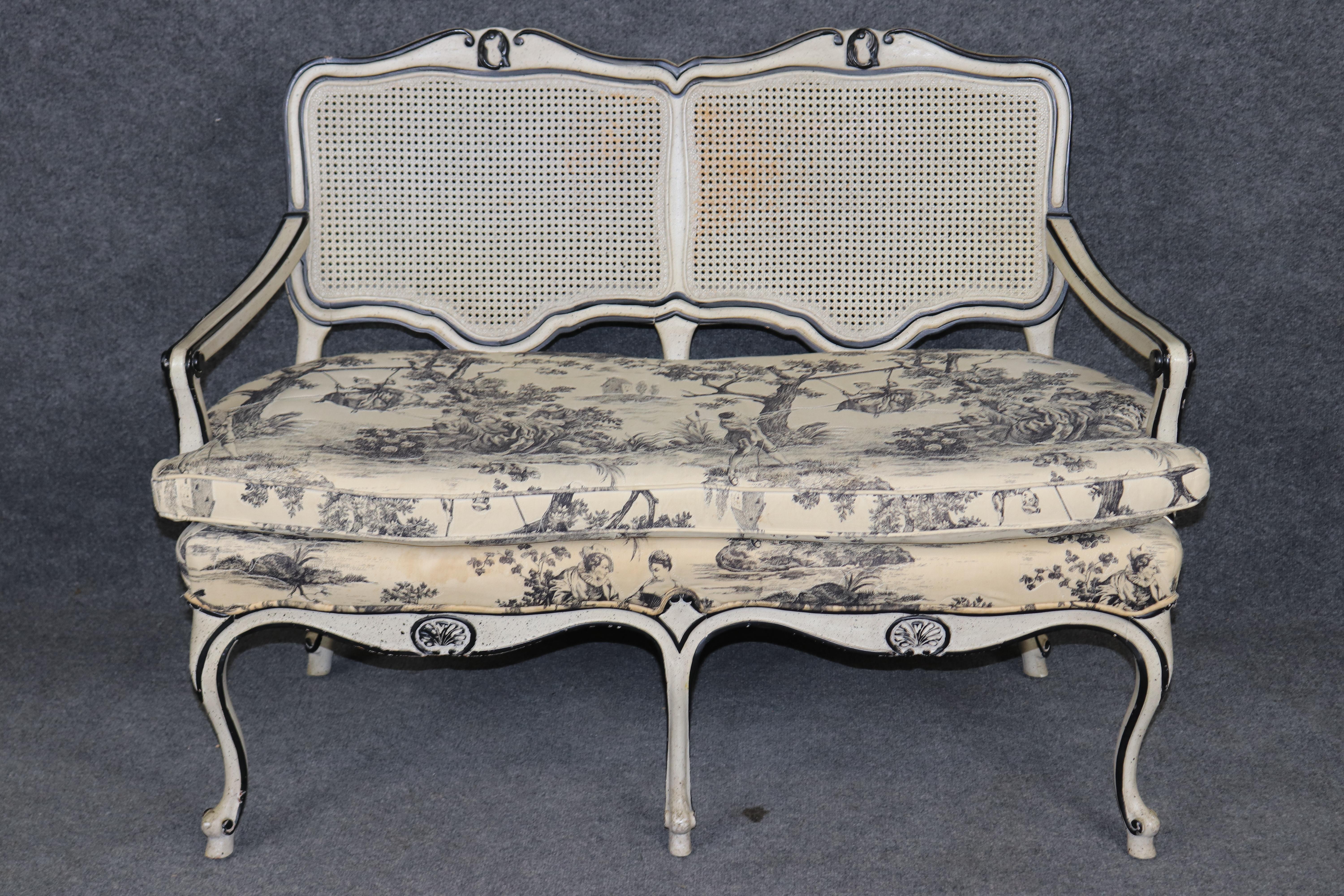 Dimensions - H: 33 1/2 in W: 45 1/4 in D: 27 in SH: 19 1/2 in 

A charming Country Louis XV-style crème paint decorated cane-back settee, exuding rustic French elegance and timeless appeal. This beautifully crafted piece features a gracefully curved