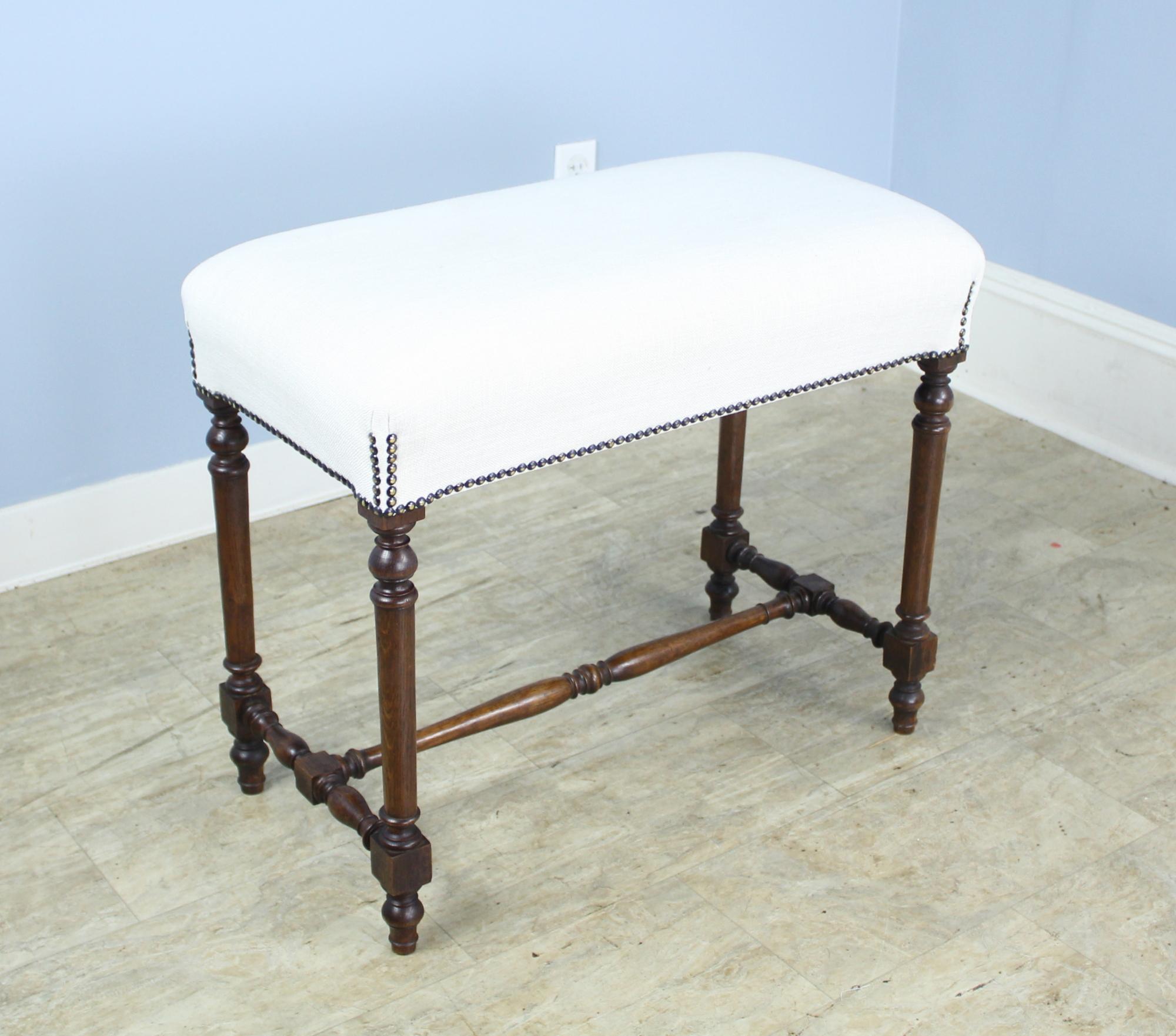An elegant country stool with nice turned legs and a slightly higher than average loft. Nicely upholstered in cream linen and can be left as is or reupholstered. Nice nail head detail. Would work well at the end of the bed, as a hall perch, or under