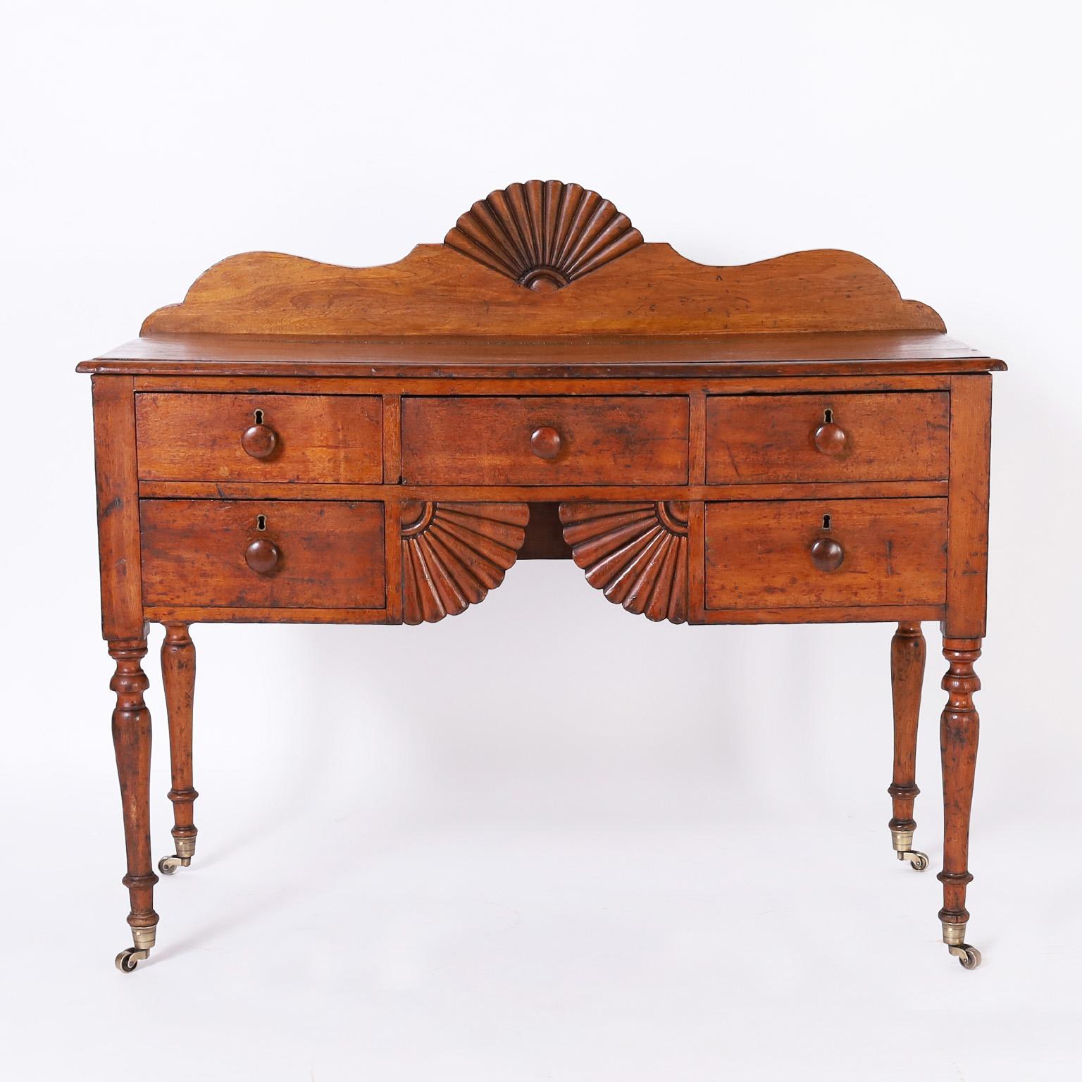Charming early 19th century server handcrafted in mahogany with classic fan carvings on the backsplash and case front, five drawers and elegant turned legs on brass casters.