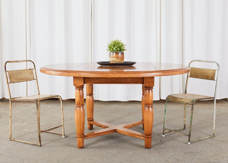 Rustic Country provincial farmhouse style round dining table featuring a 60 inch round solid pine top. The thick top is supported by large turned legs conjoined by a cross stretcher. The legs have peg joinery and the table has a subtle intentionally