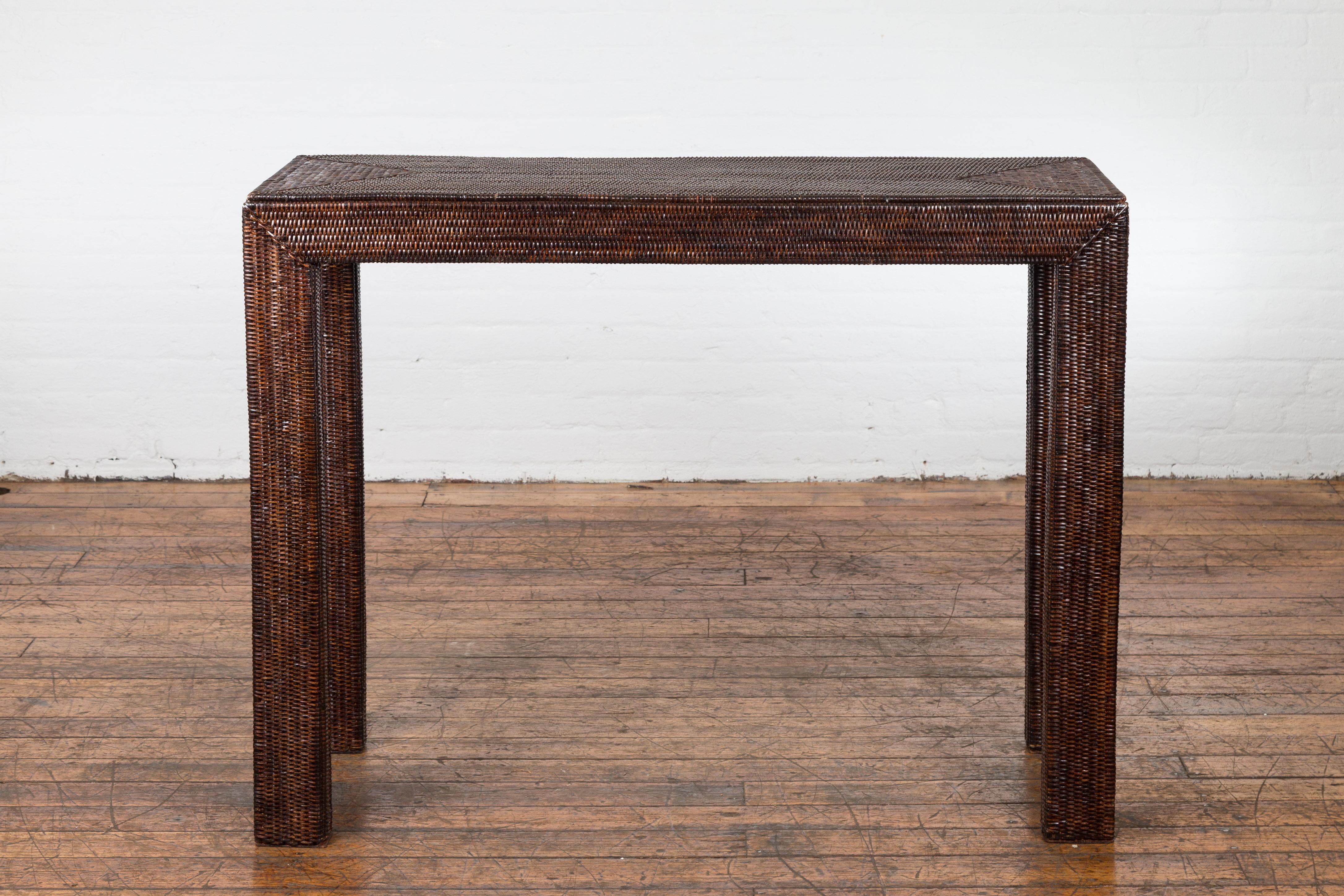 A Burmese Country style woven rattan console table from the Mid-20th Century, with straight legs, dark brown finish and triangular patterns. We currently have two tables available, the first one measuring 33 inches of height and the second one 34