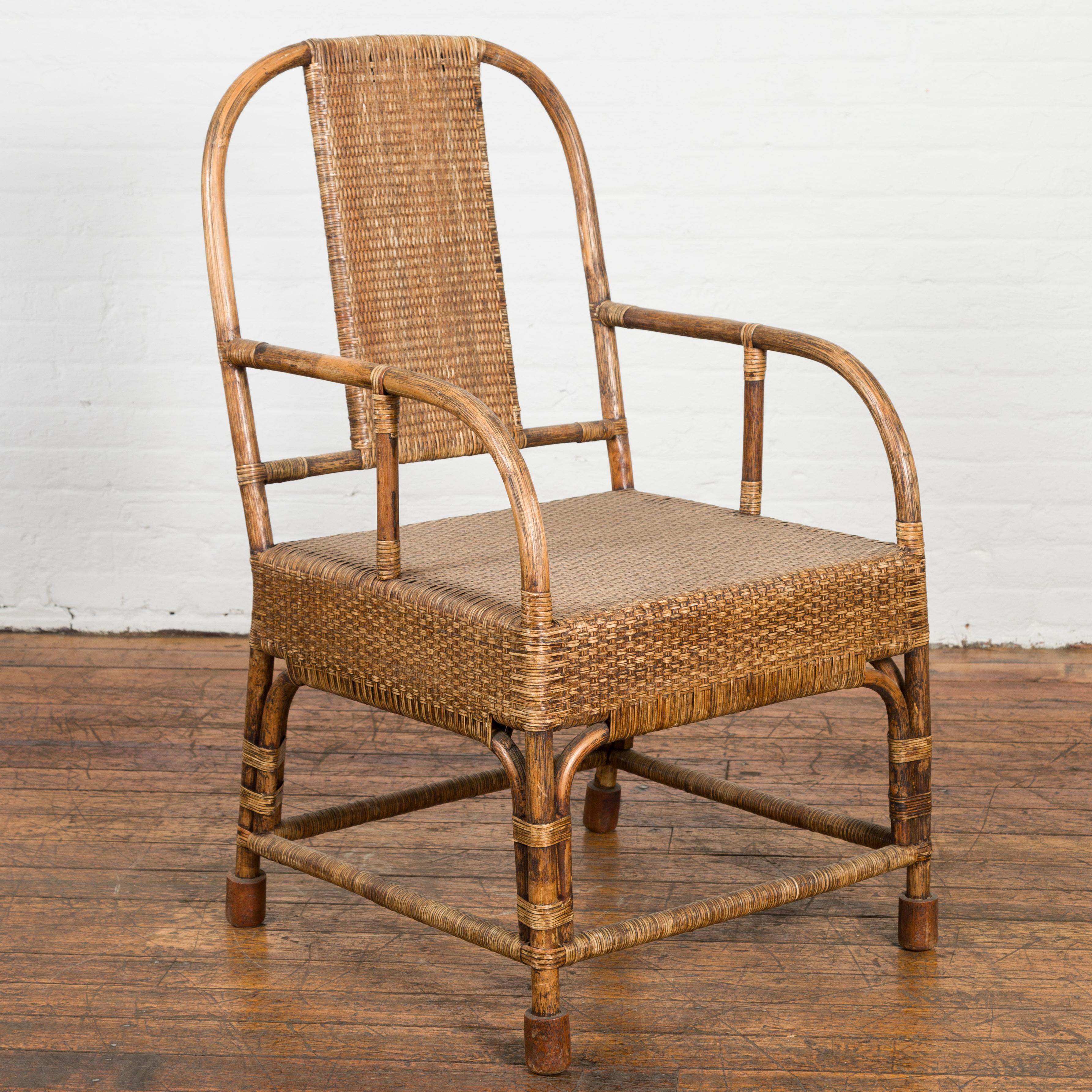 A vintage Burmese country style hand woven rattan and bamboo armchair from the mid-20th Century, with rounded open back, looping arms and side stretchers. Created in Burma during the Midcentury period, this country style bamboo armchair attracts the