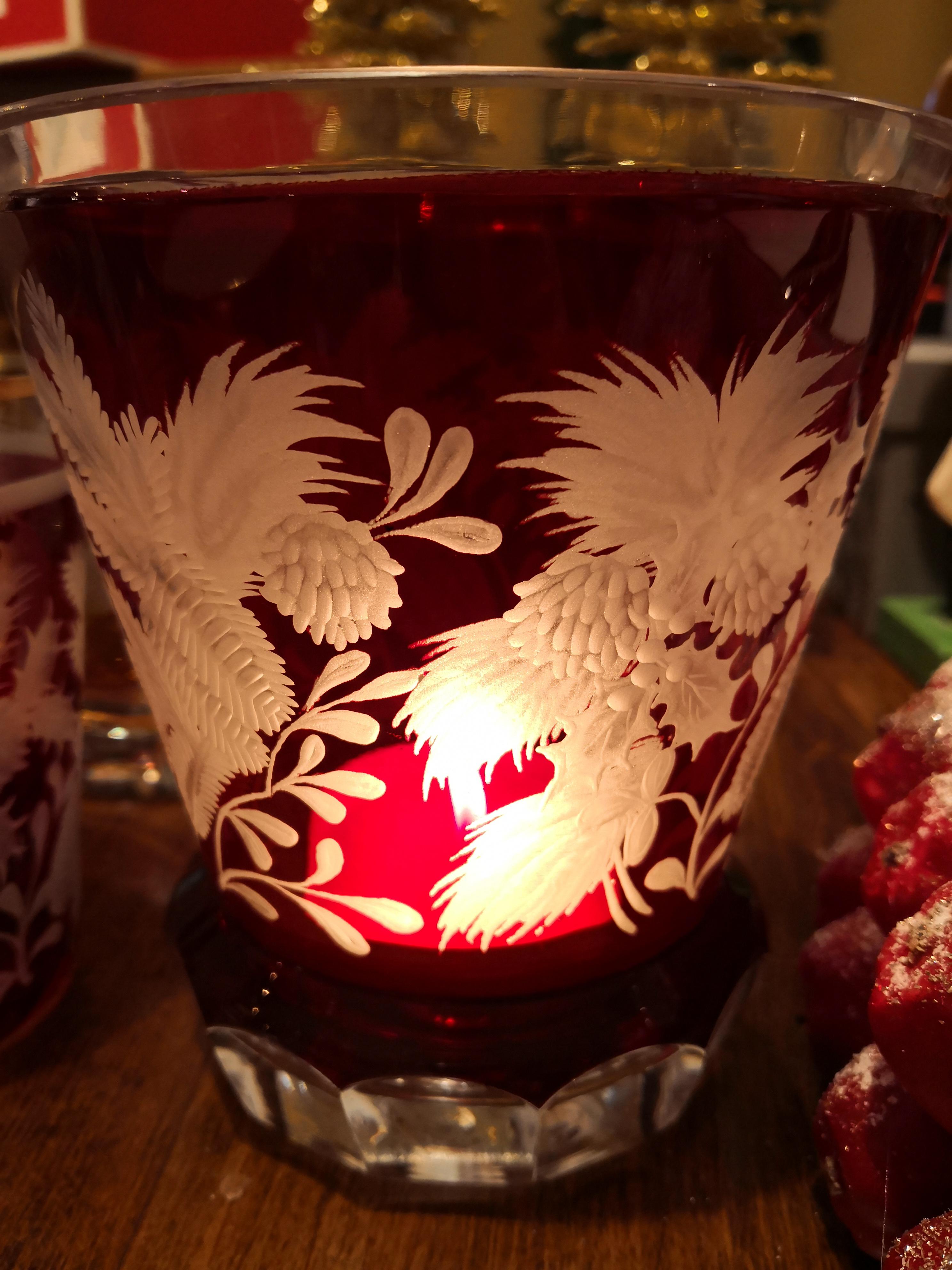 Vase/Laterne aus mundgeblasenem Kristall in leuchtend rotem Glas. Handgravur von bayerischen Glaskünstlern mit weihnachtlichem Dekor. Eine reiche Girlande aus Tannen- und Kiefernzapfen schmückt dieses Kristallgefäß. Kann mit einer Kerze als Laterne