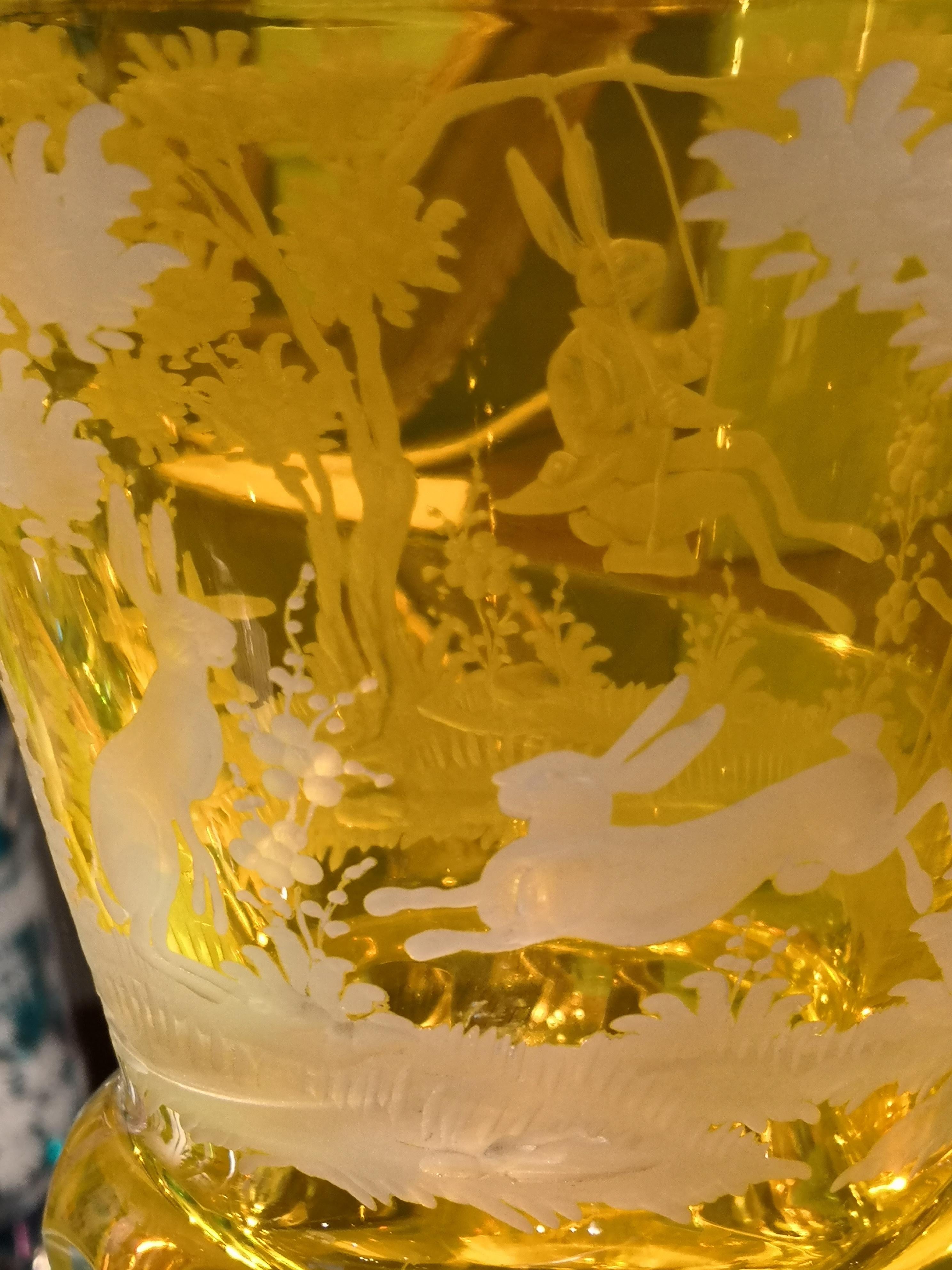 Hand blown crystal vase in yellow glass with a antique country style Easter design. Hand carved by Bavarian glass artists . A rich garland of trees and flowers with rabbits all around. One rabbit sitting on a see-saw and two smaller rabbits decorate