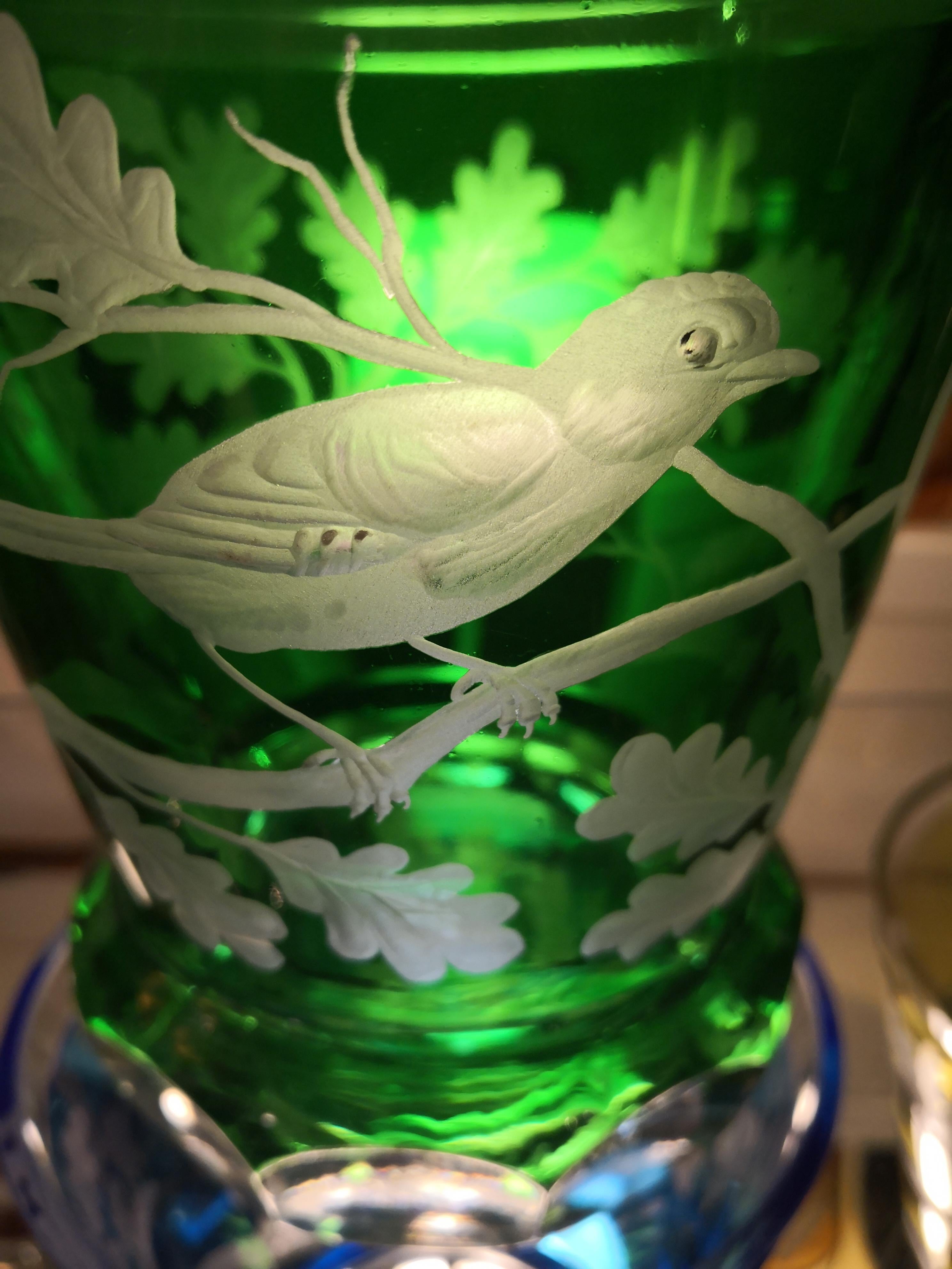 Vase/laterne en cristal soufflé à la main en verre vert avec décor d'oiseaux tout autour. Le décor montre des oiseaux assis sur des arbres et des feuilles tout autour du verre. Le décor est gravé à la main par des artistes et le fond du verre est