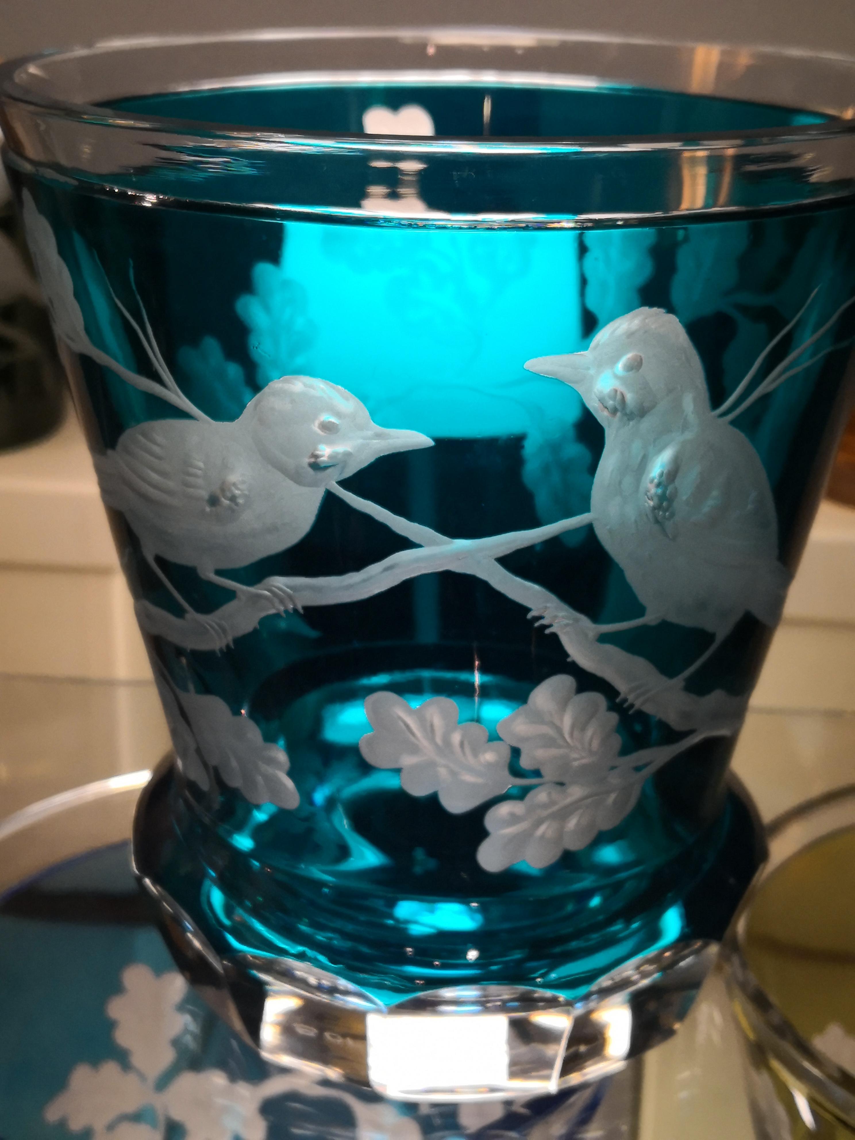Hand blown crystal vase/laterne in blue glass with birds sitting on a tree and leaves all around. The decor is hands free engraved and the glass bottom is hand-carved by glass artists. The glass here shown in blue can be ordered in different colors.