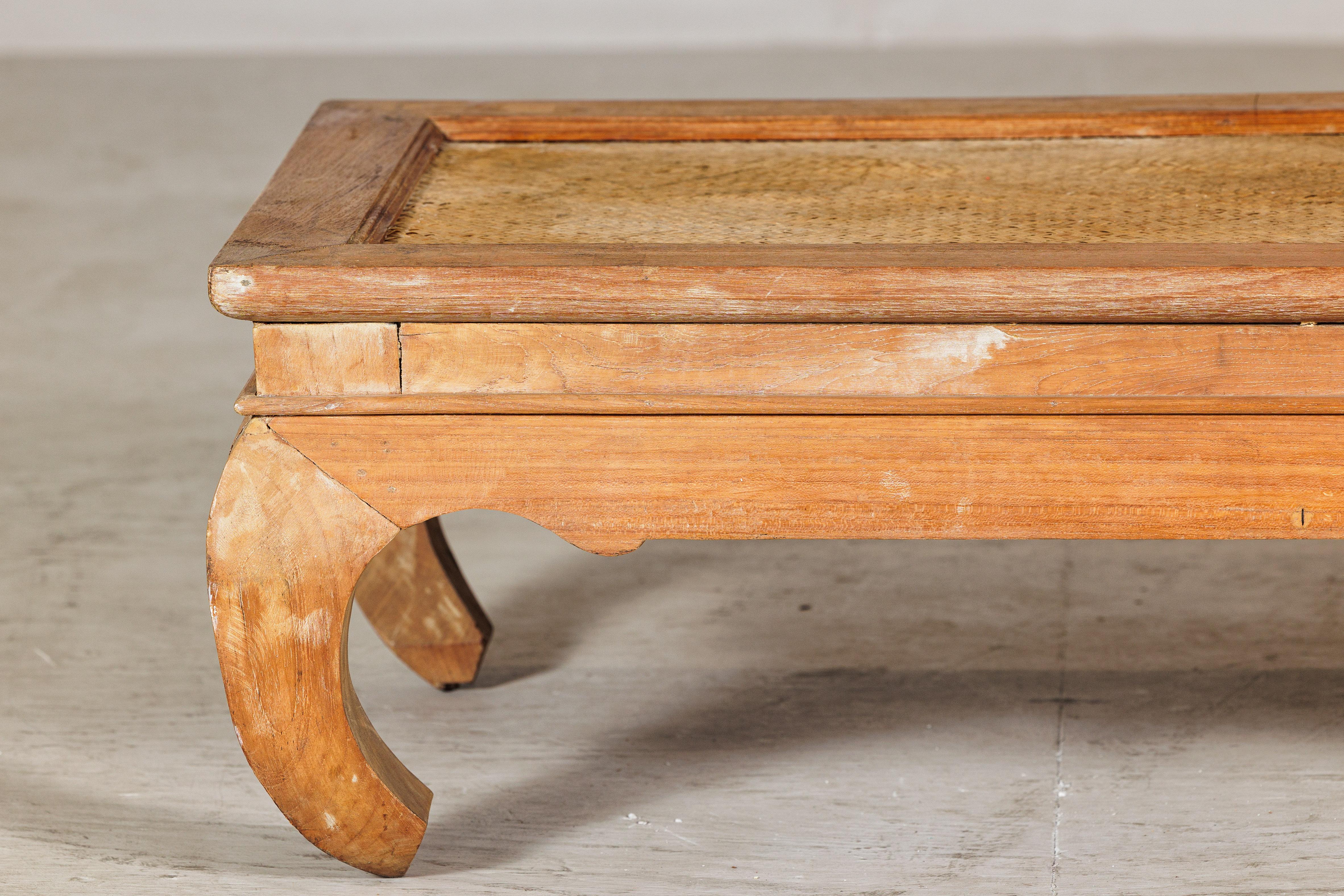 This low vintage coffee table blends rustic character with sculptural form, featuring a rectangular wooden frame set over dramatically curved legs. The top is fitted with a woven mat insert, adding texture and a relaxed, natural aesthetic. Crafted