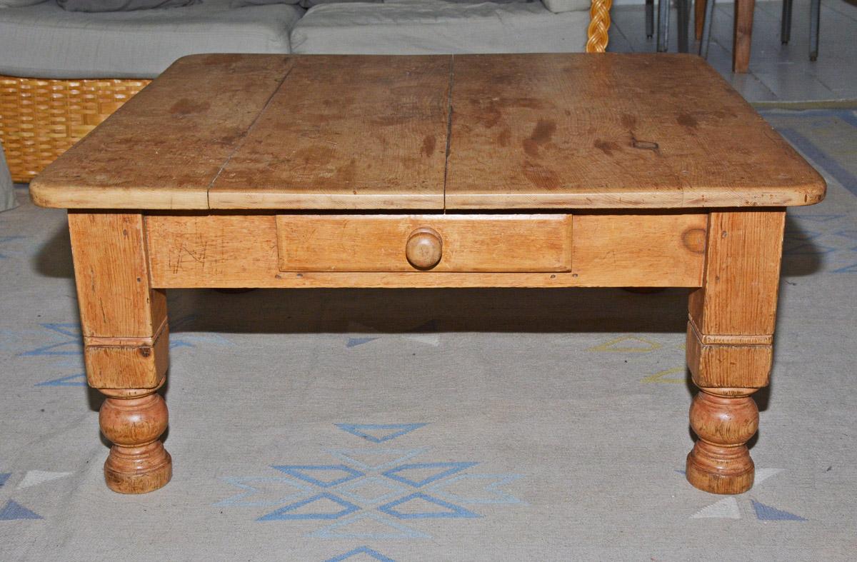 Rustic country-style pine coffee table has a square plank top with rounded corners secured to turned legs and aprons. A single drawer completes the design. Contemporary living with a rustic touch.
