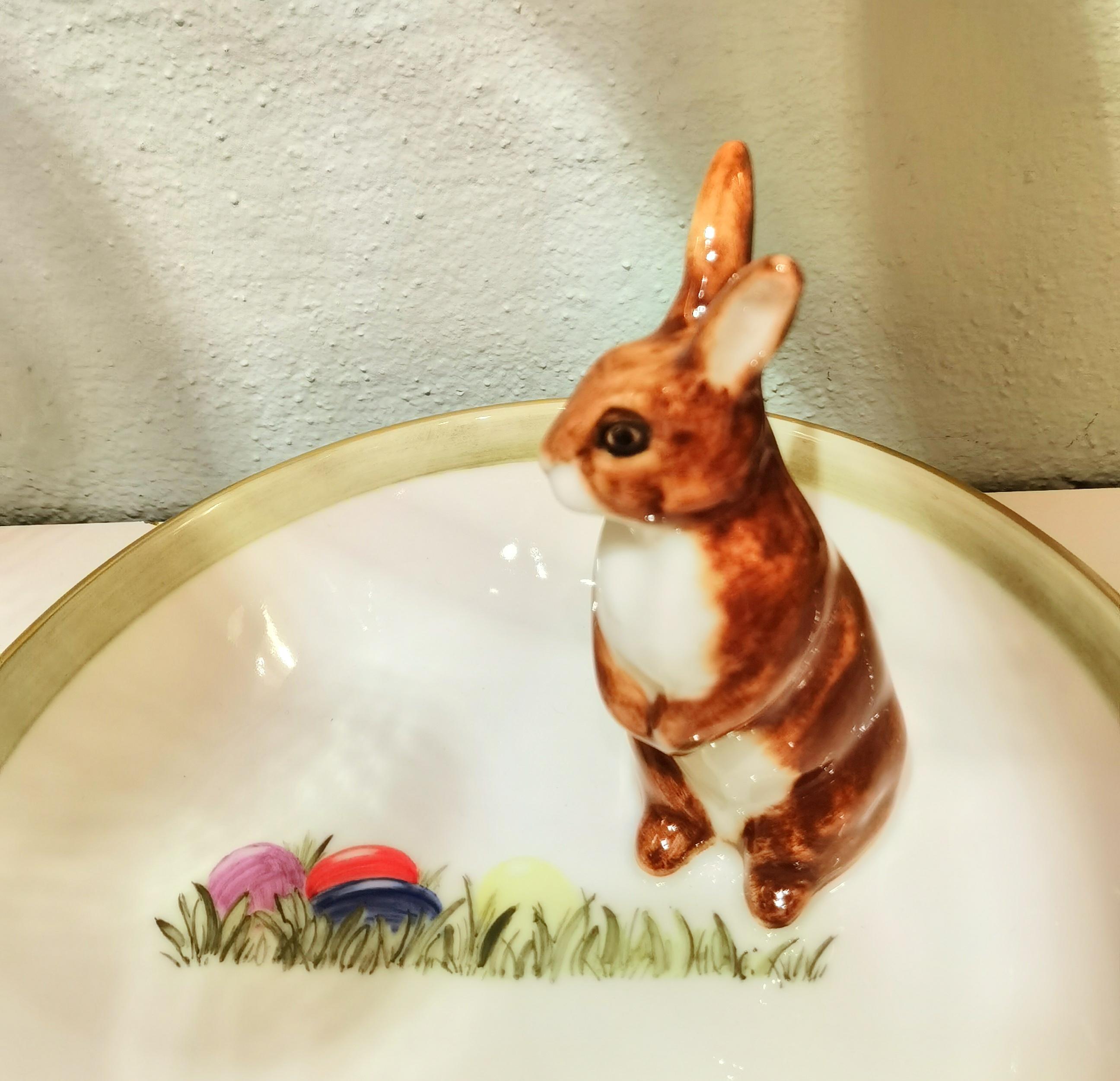 Completely handmade porcelain bowl with a hands-free naturalistic painted bunny figure in brown color in country style. The bunny is sitting at the side of the bowl for decorating nuts or sweets around. Hands-free painted with colred eggs at the