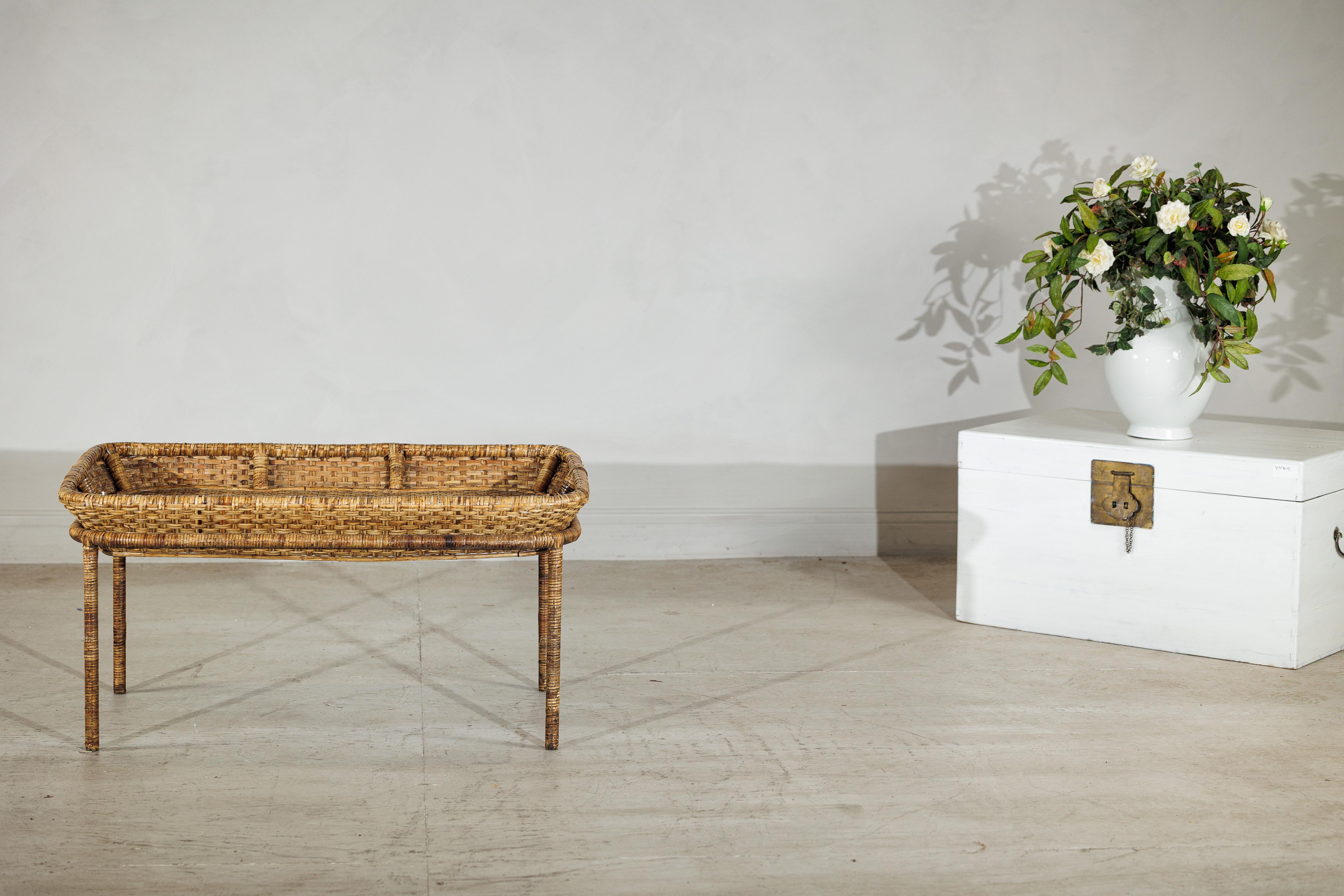 Evocando un senso di rilassato fascino country, questo tavolino vintage unisce l'artigianato al design pratico. Il pezzo è caratterizzato da un ampio e poco profondo piano in rattan, la cui superficie intrecciata a mano presenta sottili variazioni